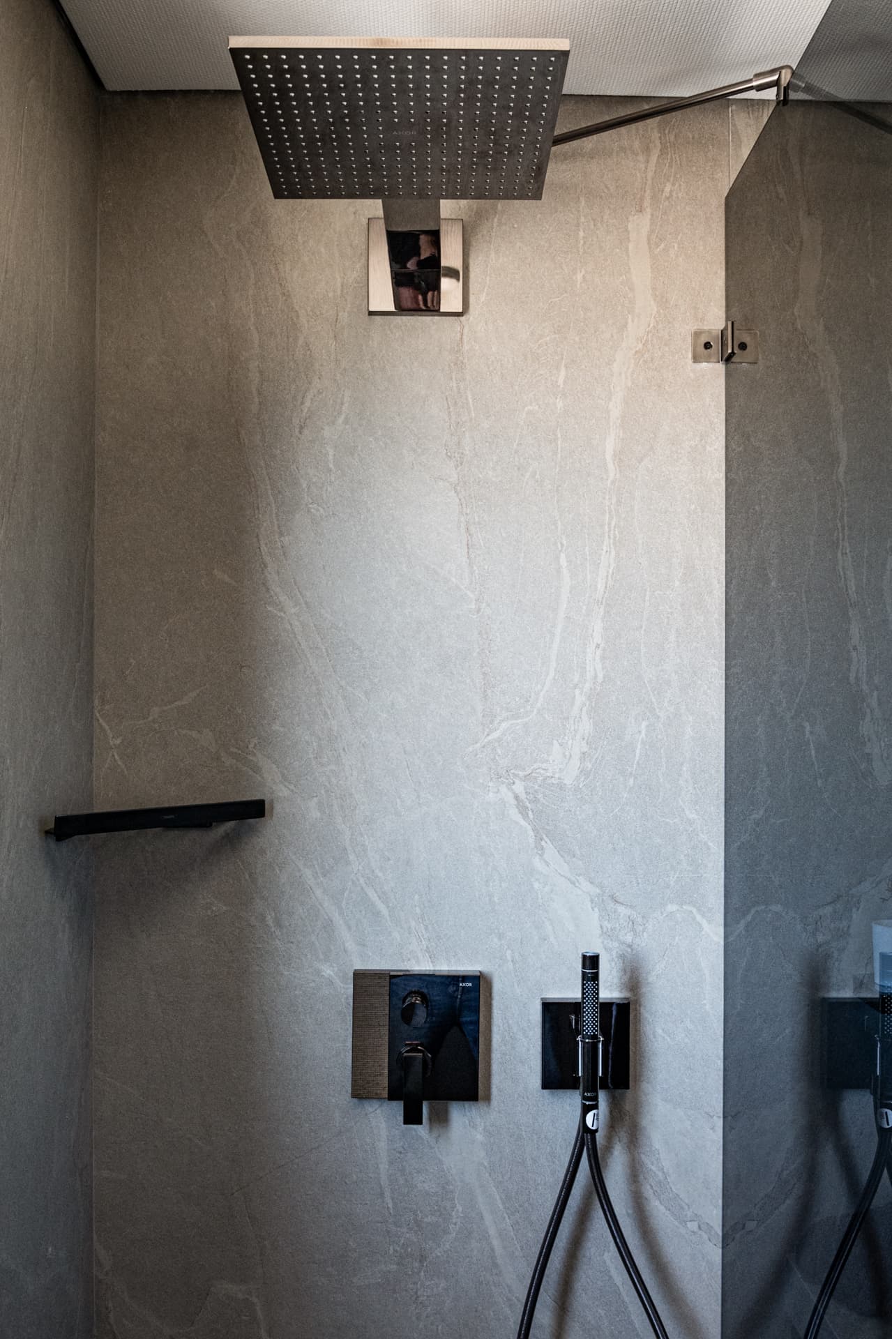 Opposite shower wall with square rain head, black mixer, hand shower and slim shelf in the master bathroom of Khayyal