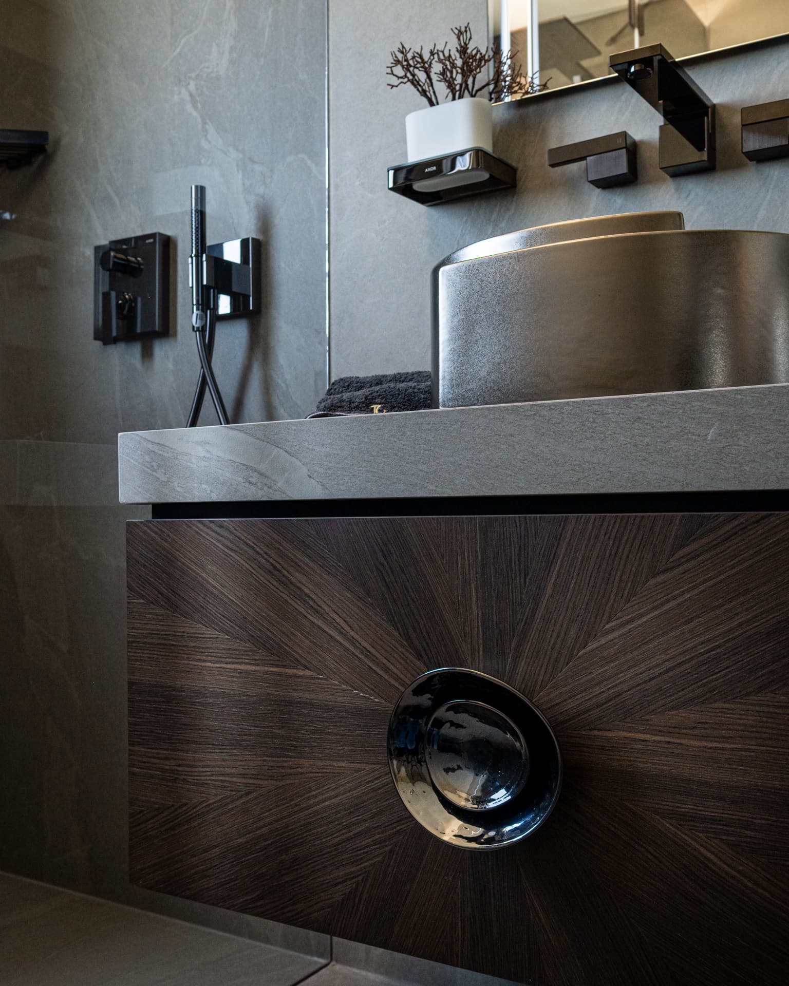 Low angle on a sunburst walnut vanity drawer with a glossy black round pull under a metallic basin in the master bathroom of Khayyal
