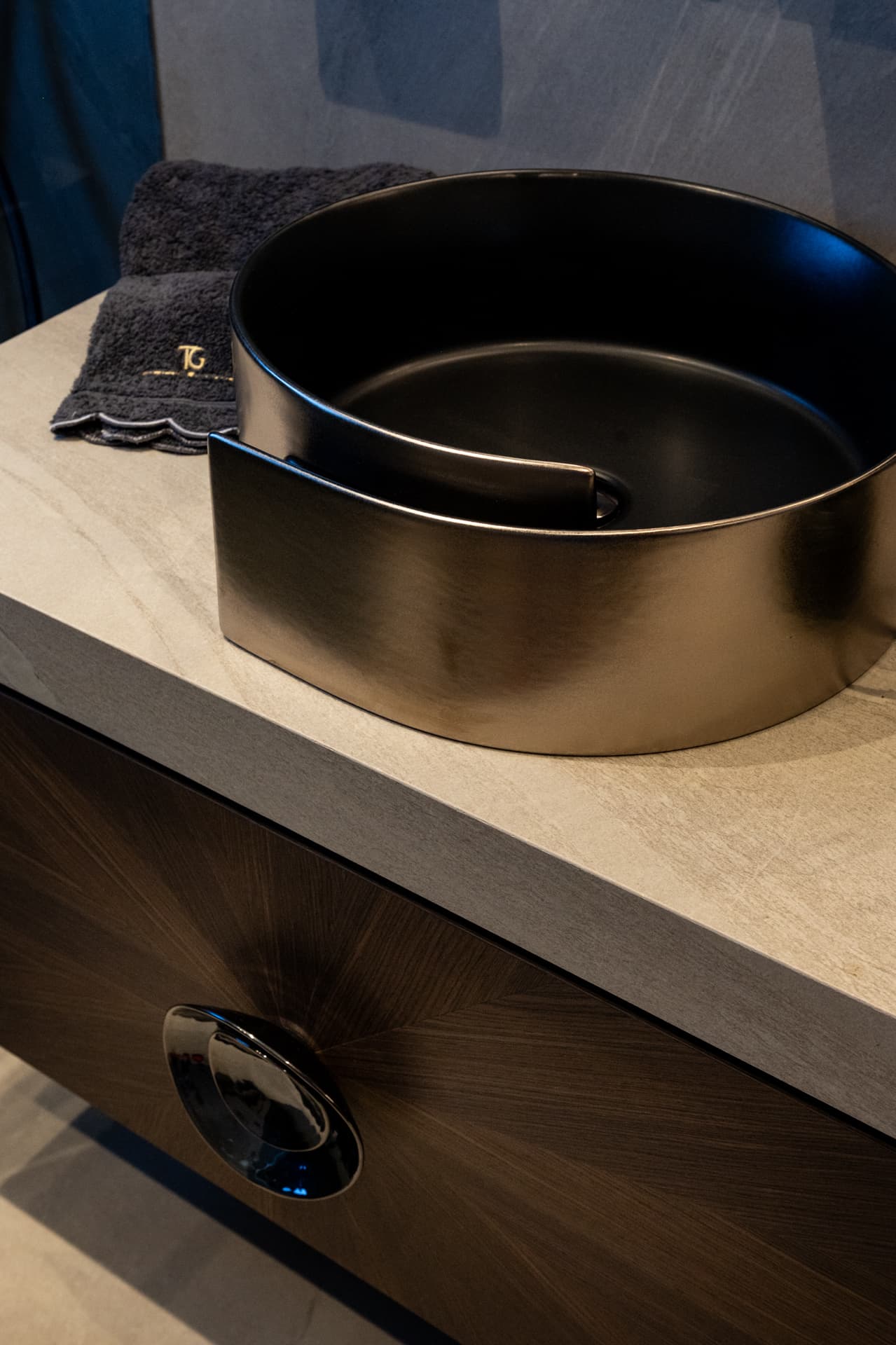 Dark metallic wrap-around vessel basin on a stone countertop above the walnut vanity in the master bathroom of Khayyal