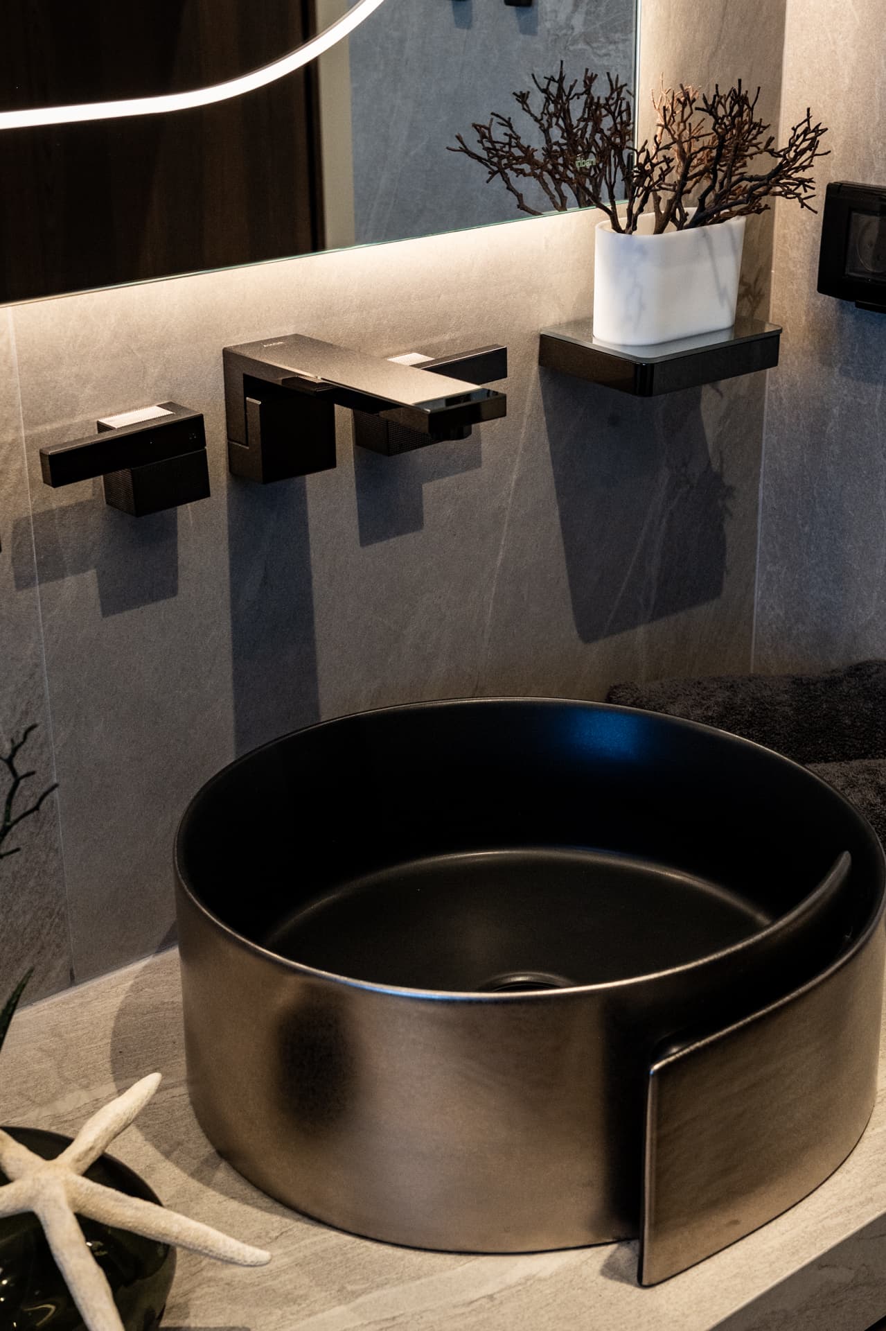 Black wall-mounted tap above a curled metallic vessel basin with coral and starfish decor in the master bathroom of Khayyal