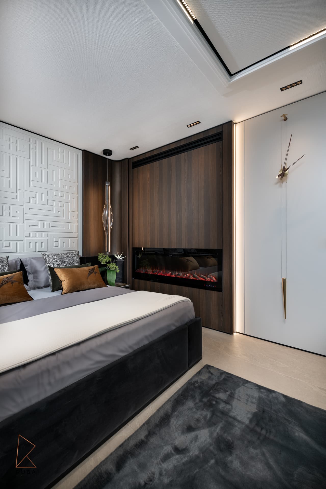 Angled view of the bed, walnut fireplace wall and a slim oversized wall clock in the master bedroom of Khayyal