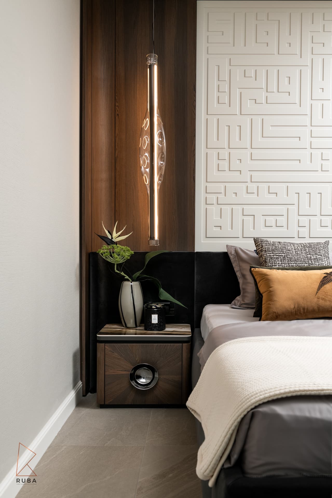 Slim glass pendant light over a sunburst-veneer nightstand beside the geometric relief headboard in the master bedroom of Khayyal