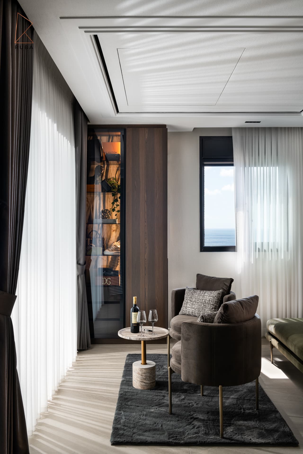 Sitting corner with a brown upholstered armchair, stone side table and sheer curtains in the master bedroom of Khayyal