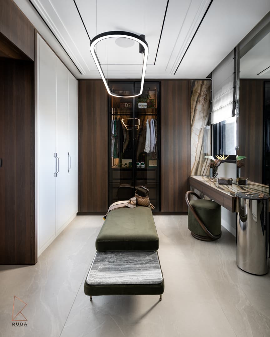 Dressing room with a green velvet bench, glass wardrobe, veined stone vanity wall and an oval ring pendant in Khayyal