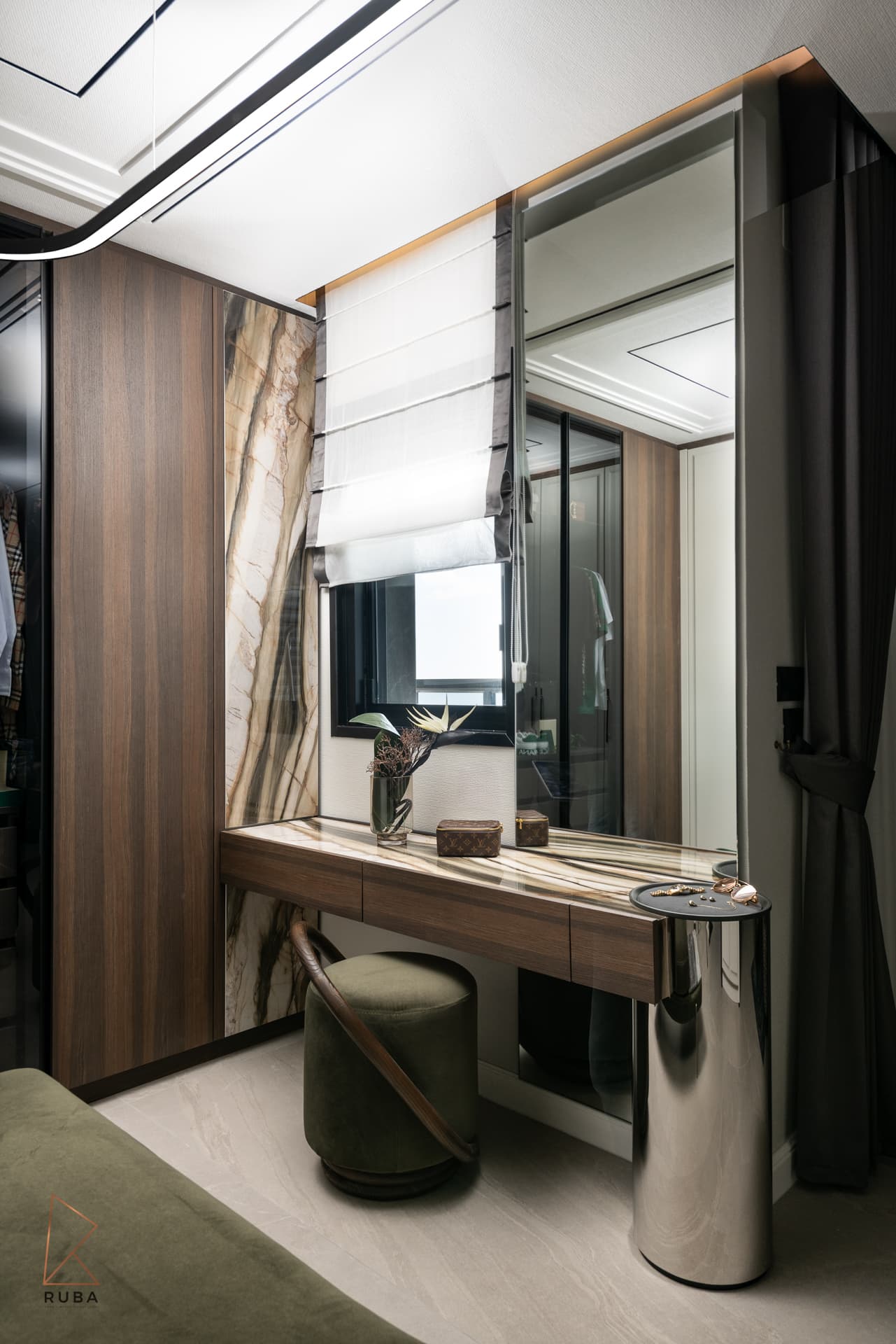 Vanity desk with a green velvet stool, steel column and bold veined stone panel under a Roman blind in the dressing room of Khayyal