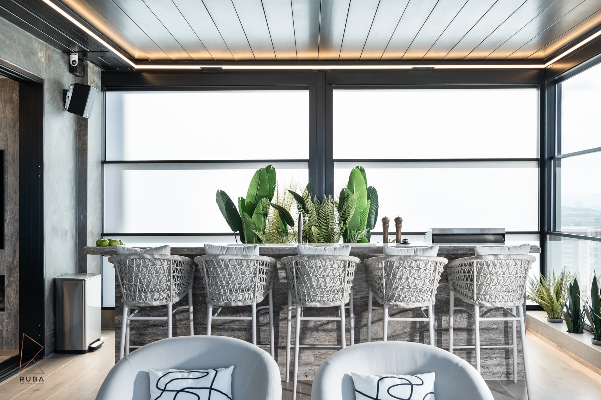 Terrace bar with woven white stools and tropical plants under a lit pergola ceiling in the outdoor area of Khayyal