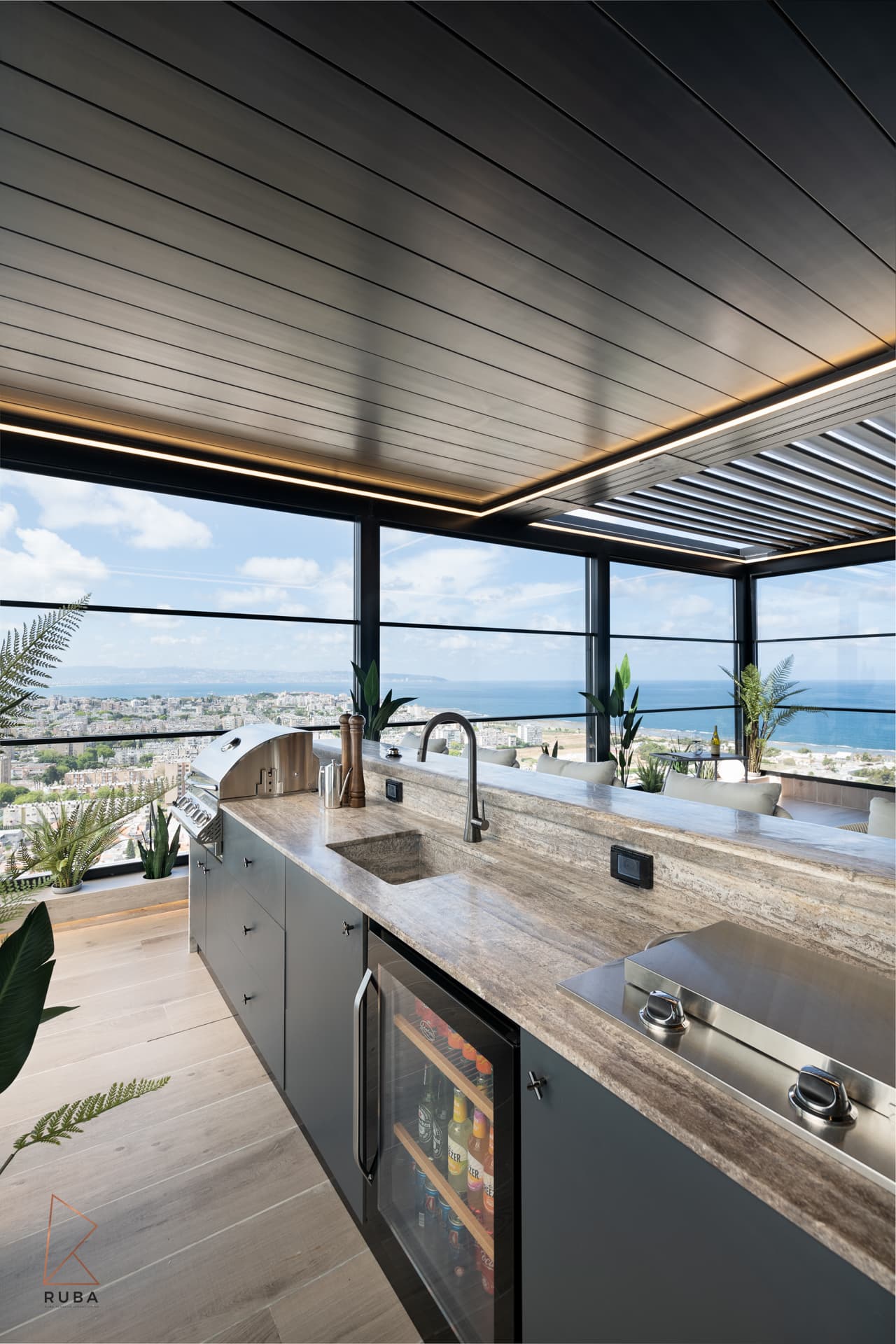 Outdoor kitchen with a veined stone counter, grill, sink and glass-front drinks fridge on the terrace of Khayyal