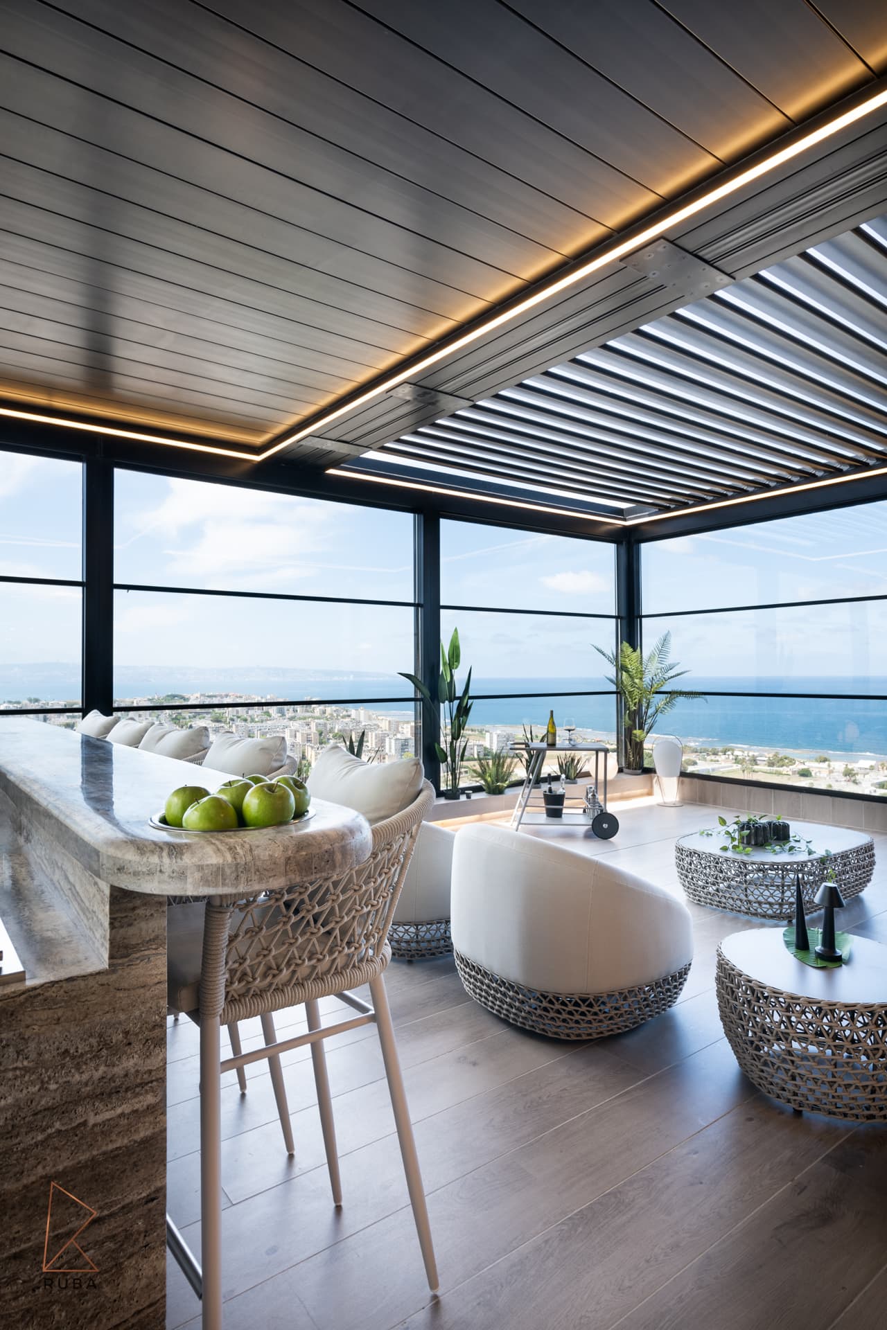 Stone bar with woven stools and white lounge chairs under a louvred pergola with panoramic sea views on the terrace of Khayyal