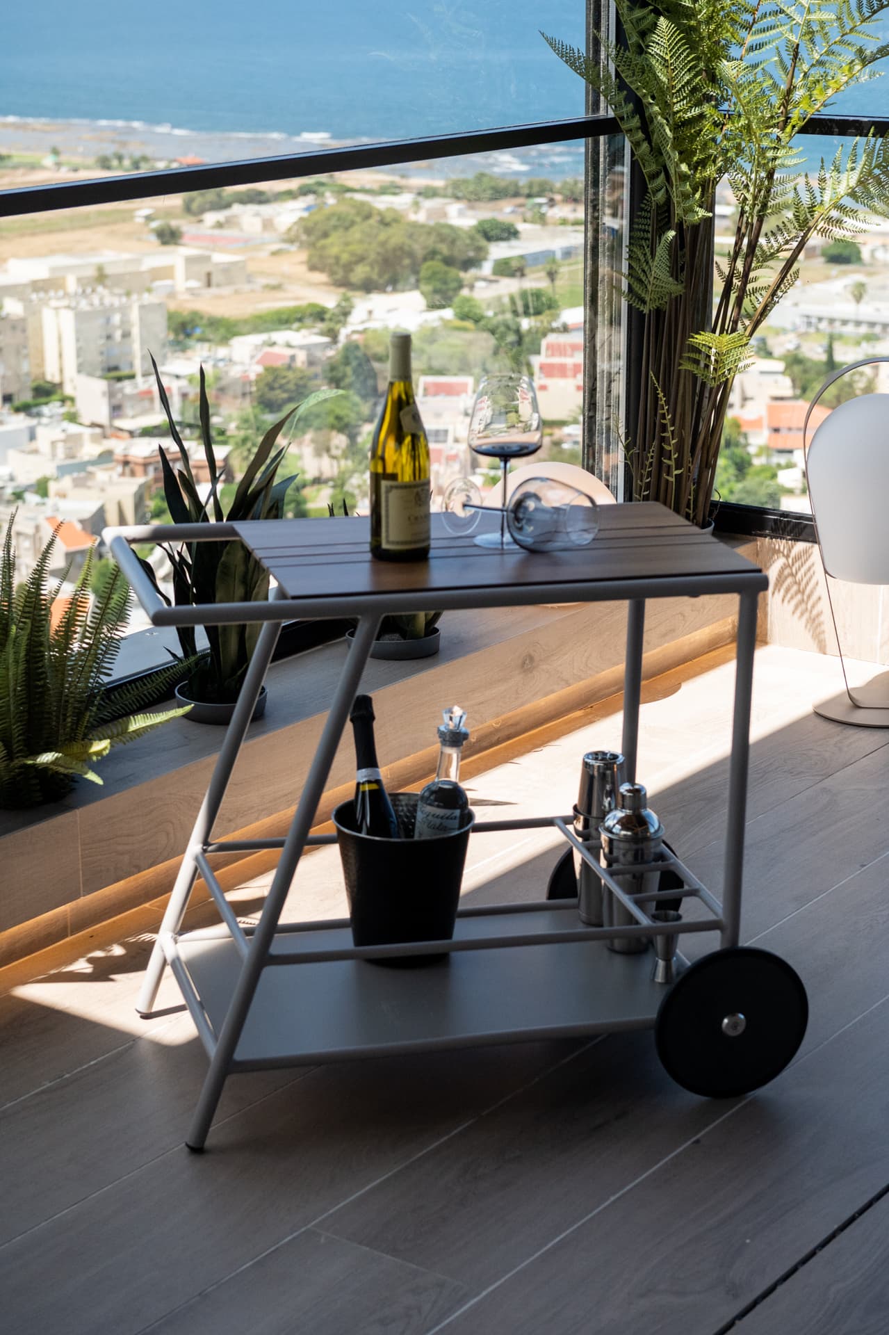 Bar cart with a wine bucket and cocktail tools beside plants and a sunny sea view on the terrace of Khayyal