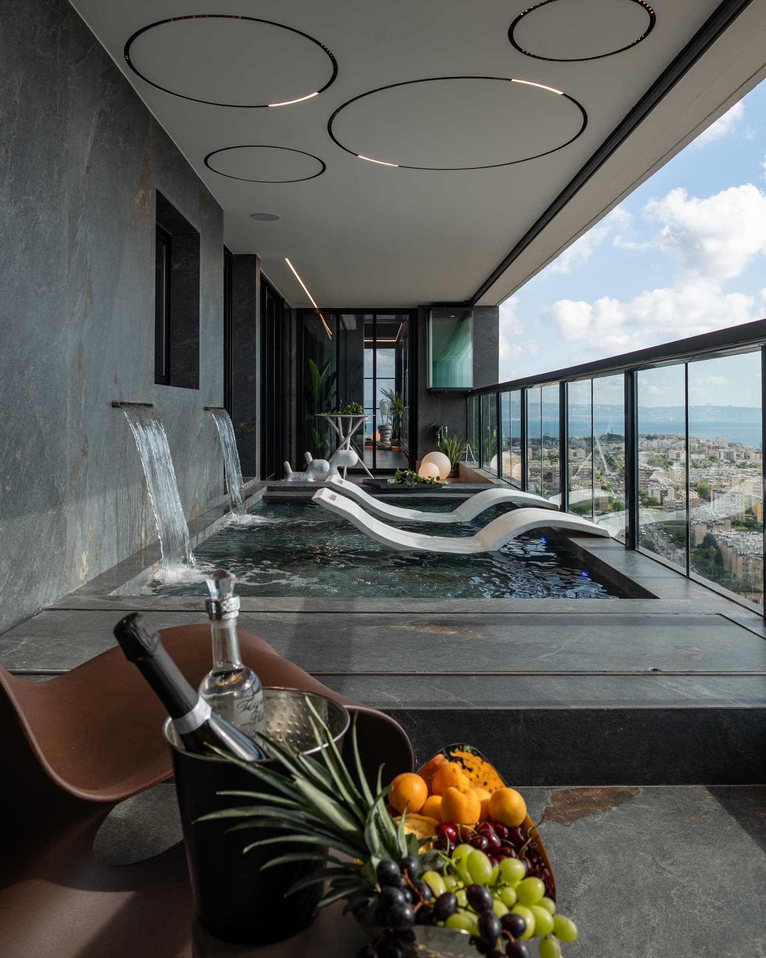 Wall spouts pouring into the terrace pool with white loungers, circular ceiling lights and a fruit bowl in front in Khayyal