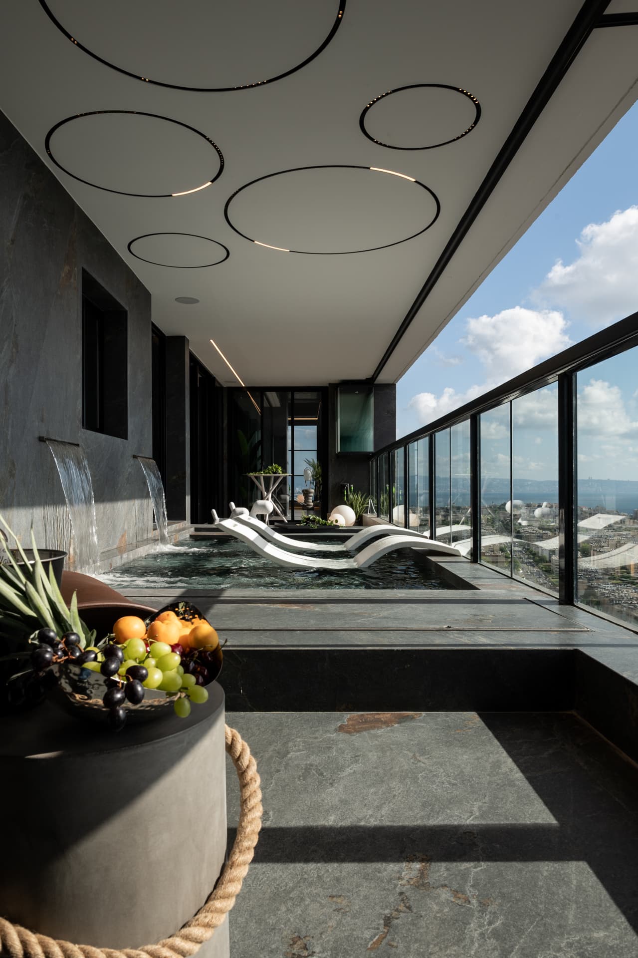 Terrace pool under ring-shaped ceiling lights, viewed past a rope-wrapped stand holding a fruit bowl in Khayyal