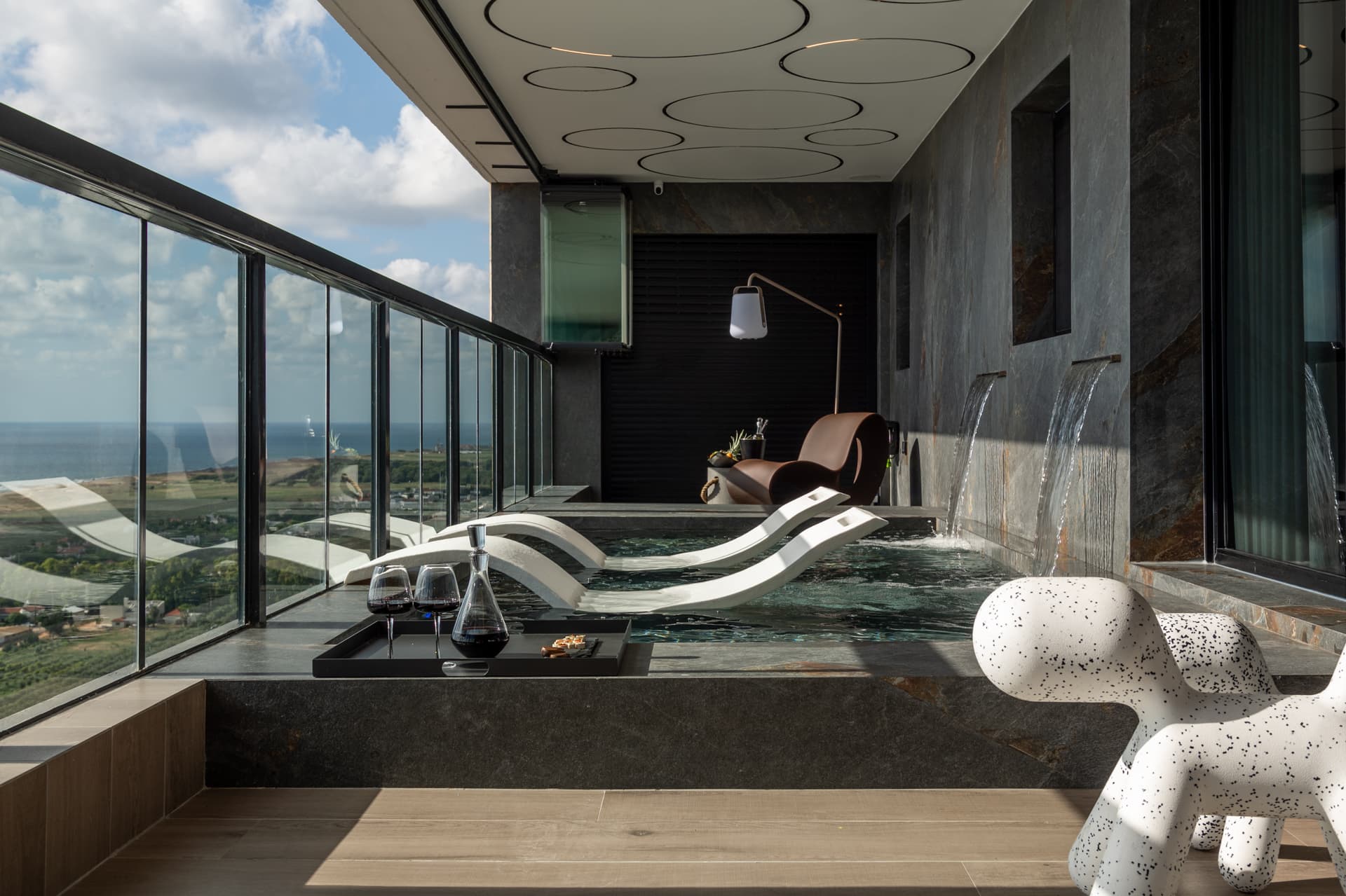 Daylight view of the terrace pool with a wine tray, white loungers and a lounge chair under a floor lamp in Khayyal