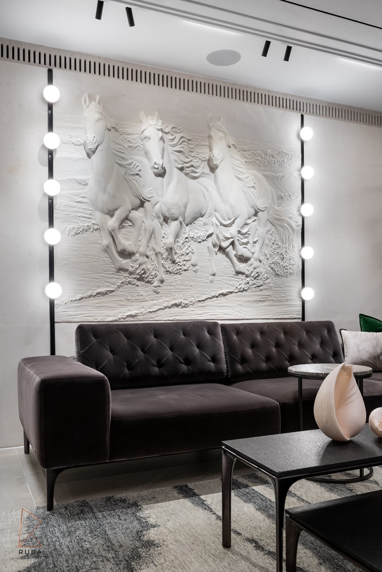 Tufted velvet sofa beneath a sculpted white horse relief wall lined with globe lights in the salon of Khayyal