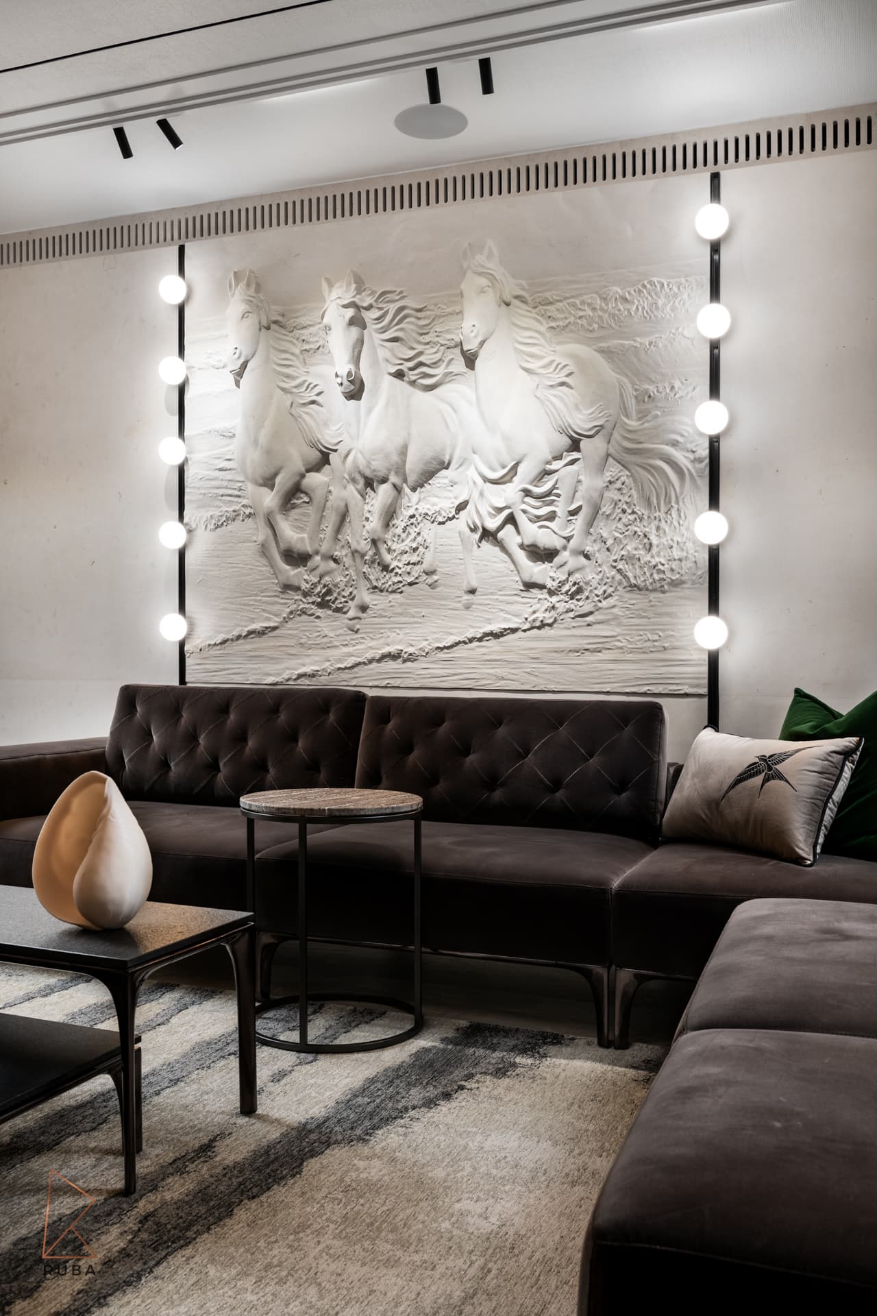 Angled view of the horse relief wall, tufted corner sofa and a shell sculpture on the black coffee table in the salon of Khayyal
