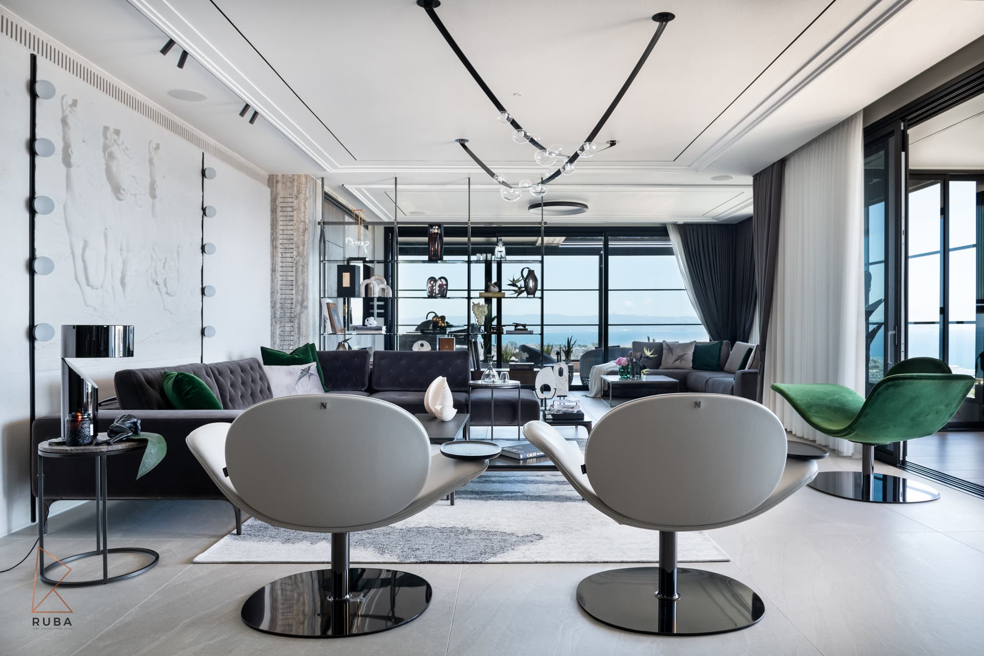 Pair of white swivel lounge chairs and a green velvet chair facing an open-plan lounge with sea-view windows in the salon of Khayyal