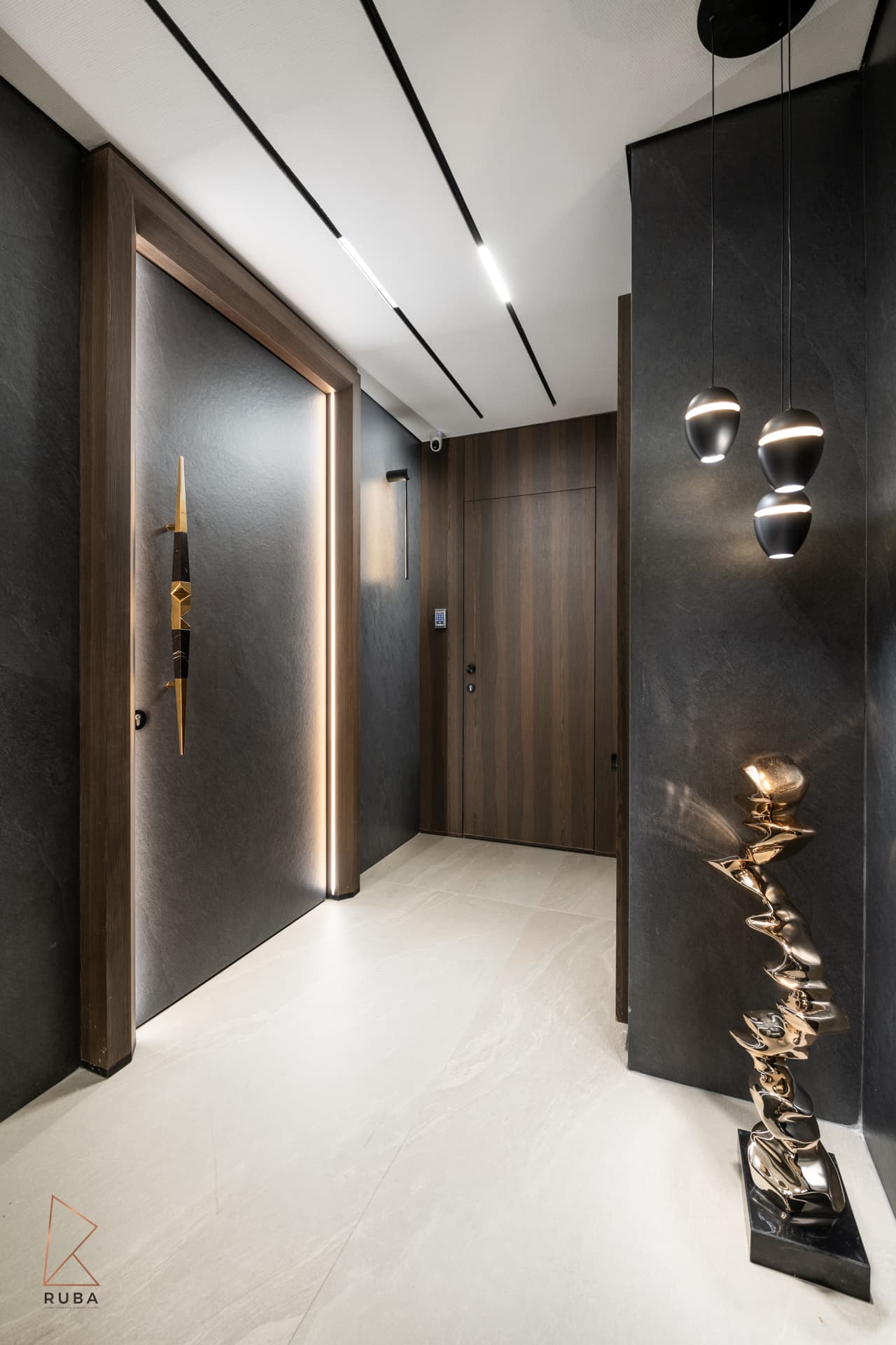Entrance hall with a lit oversized door pull, dark stone walls, black pendant lights and a twisted gold floor sculpture in Khayyal