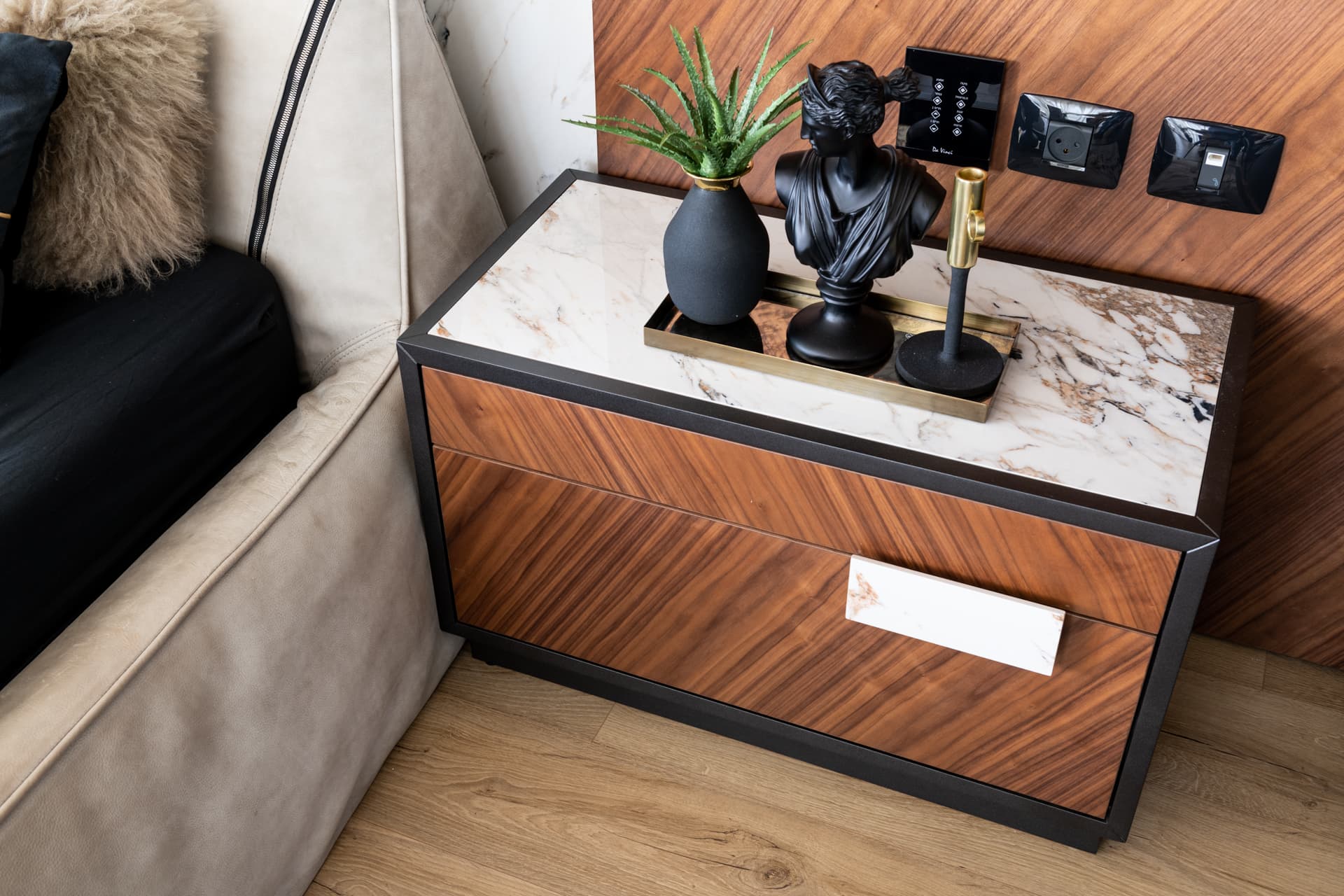 Walnut nightstand with a veined stone top and black bust sculpture beside the bed in the master bedroom of King David