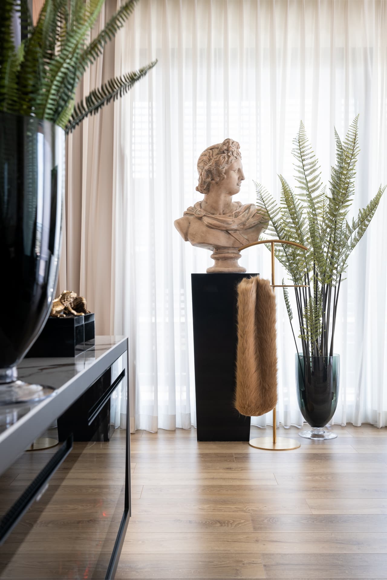 Classical bust on a black plinth, a brass stand draped with fur and a fern in a smoked glass vase in the master bedroom of King David