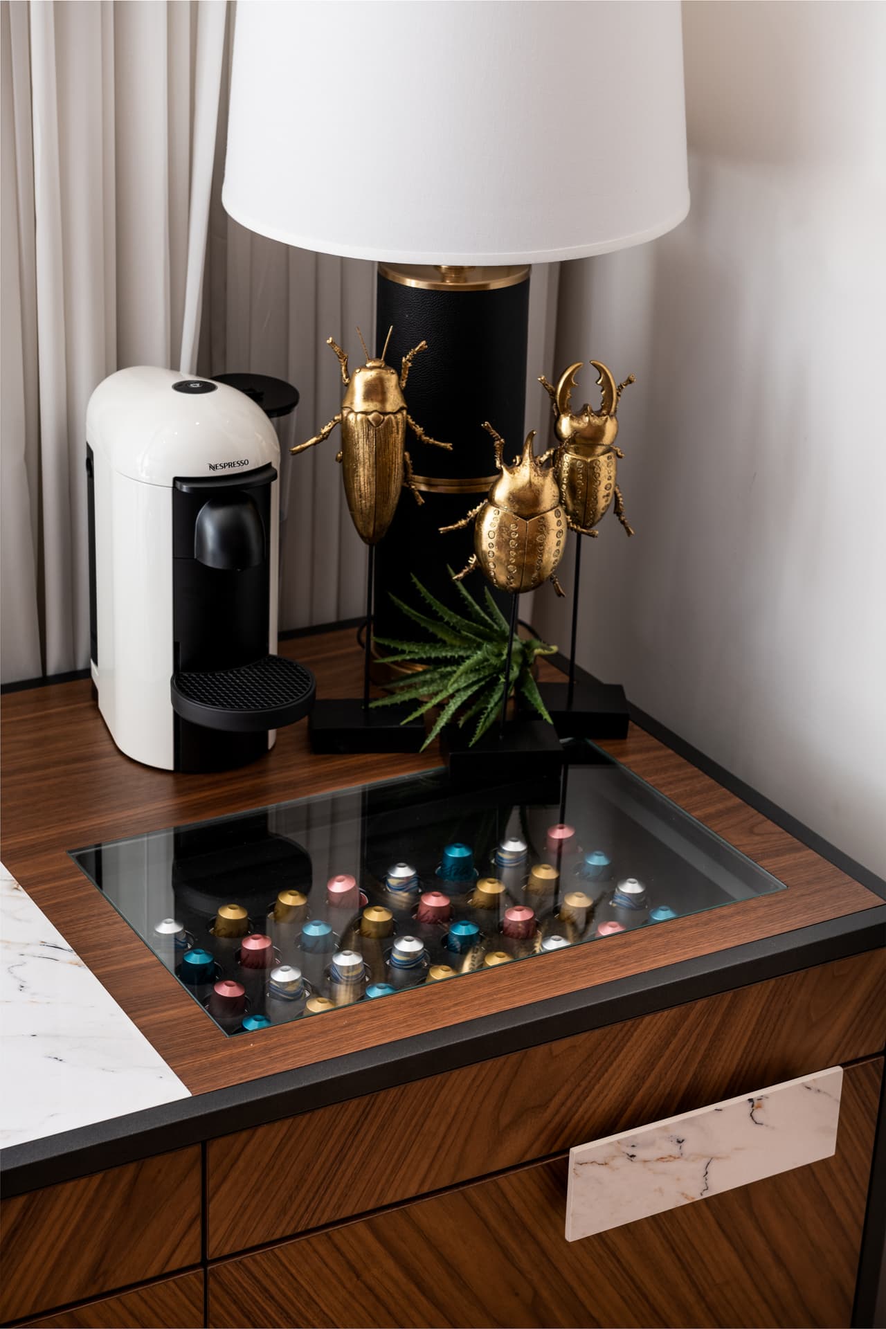 Walnut cabinet with a glass-topped capsule drawer, gold beetle sculptures and a black lamp in the home office of King David