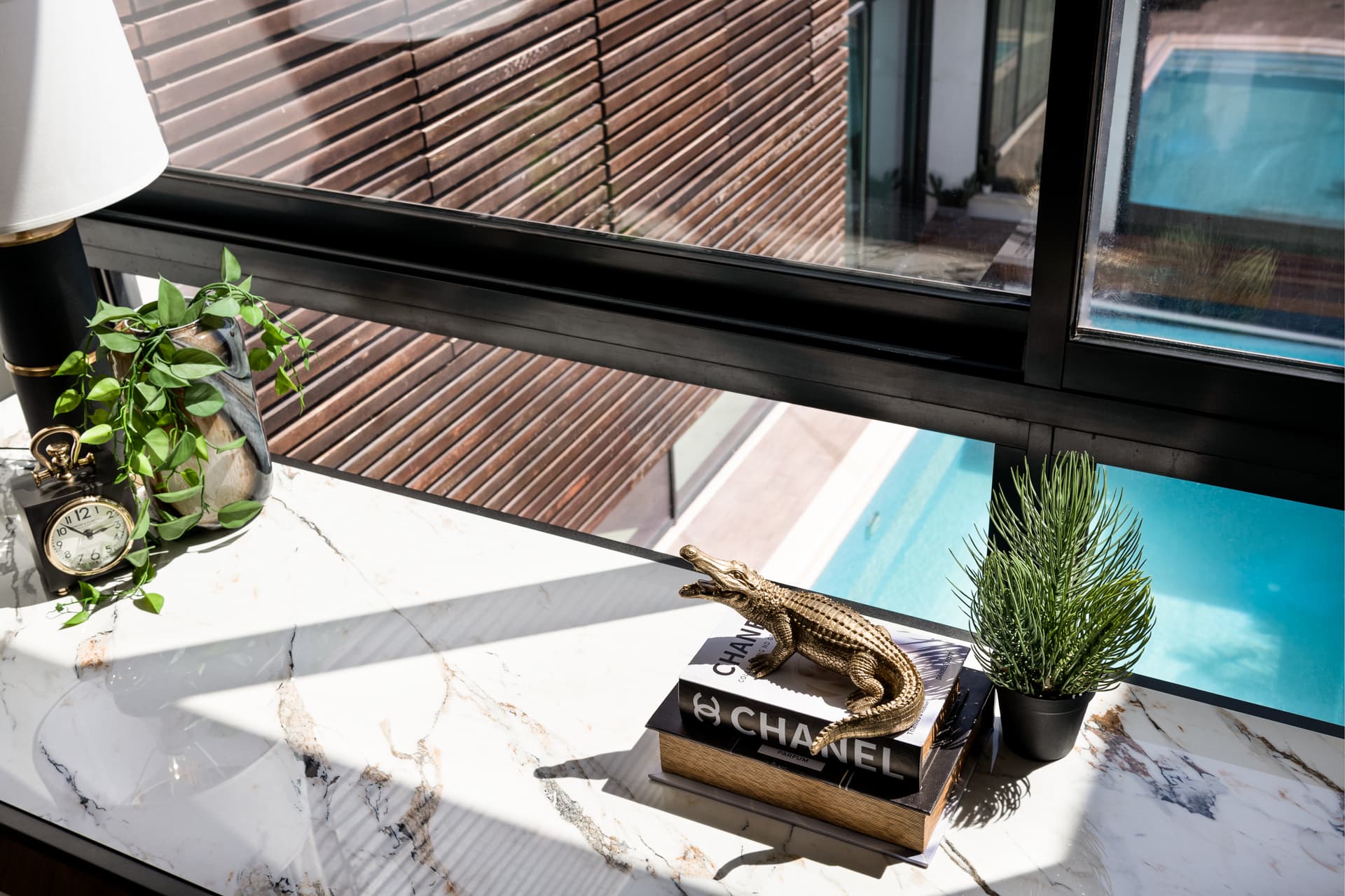Veined stone desktop with a gold crocodile figurine and plants by a window over the pool in the home office of King David
