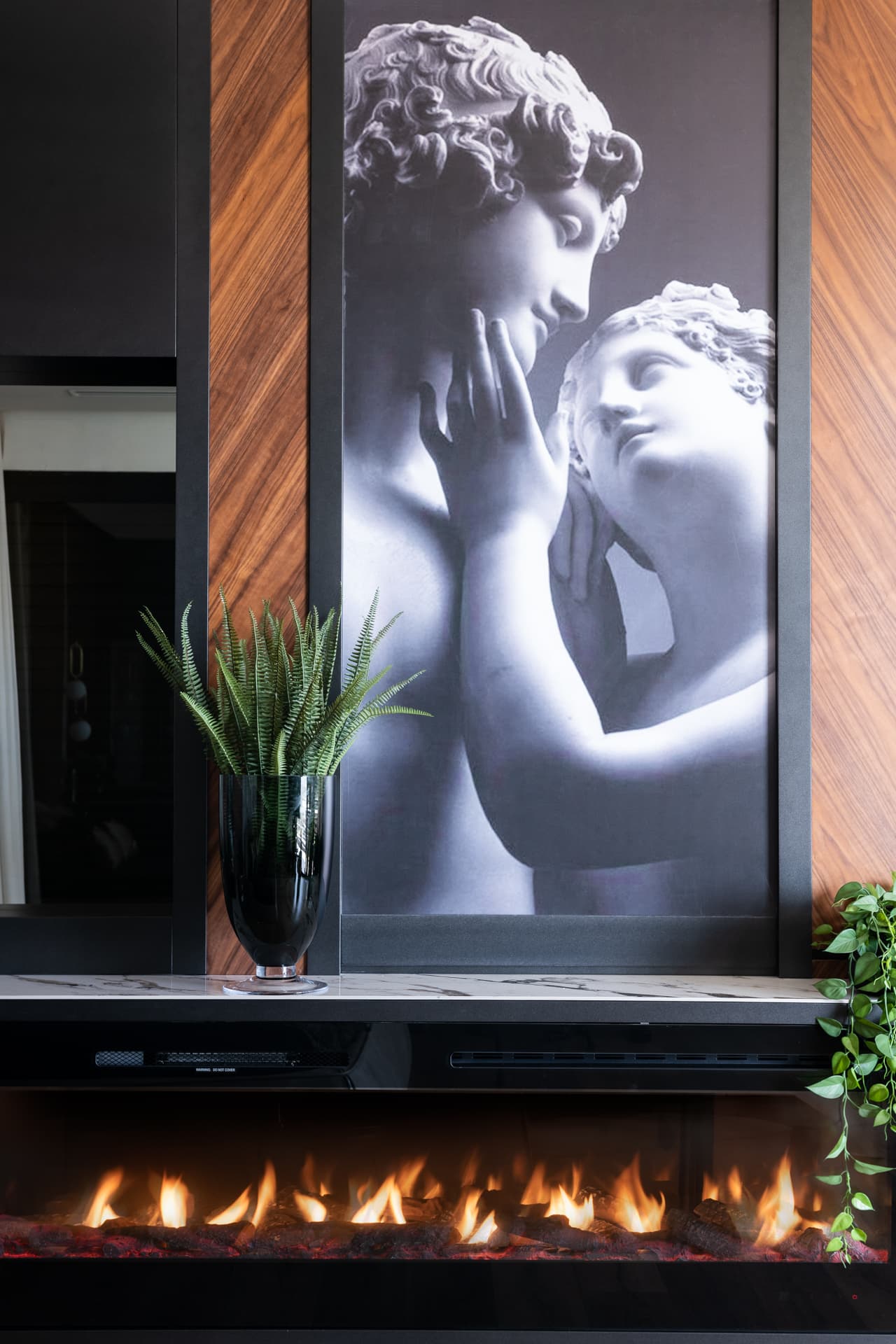 Classical sculpture print in a dark frame above a linear fireplace flanked by walnut panels in the master bedroom of King David
