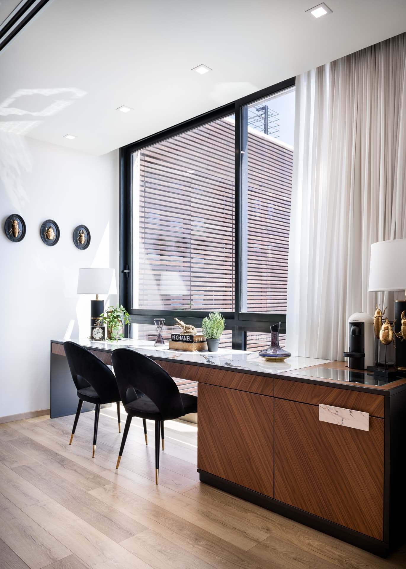Walnut desk with a veined stone top, black velvet chairs and a slatted-screen window in the home office of King David