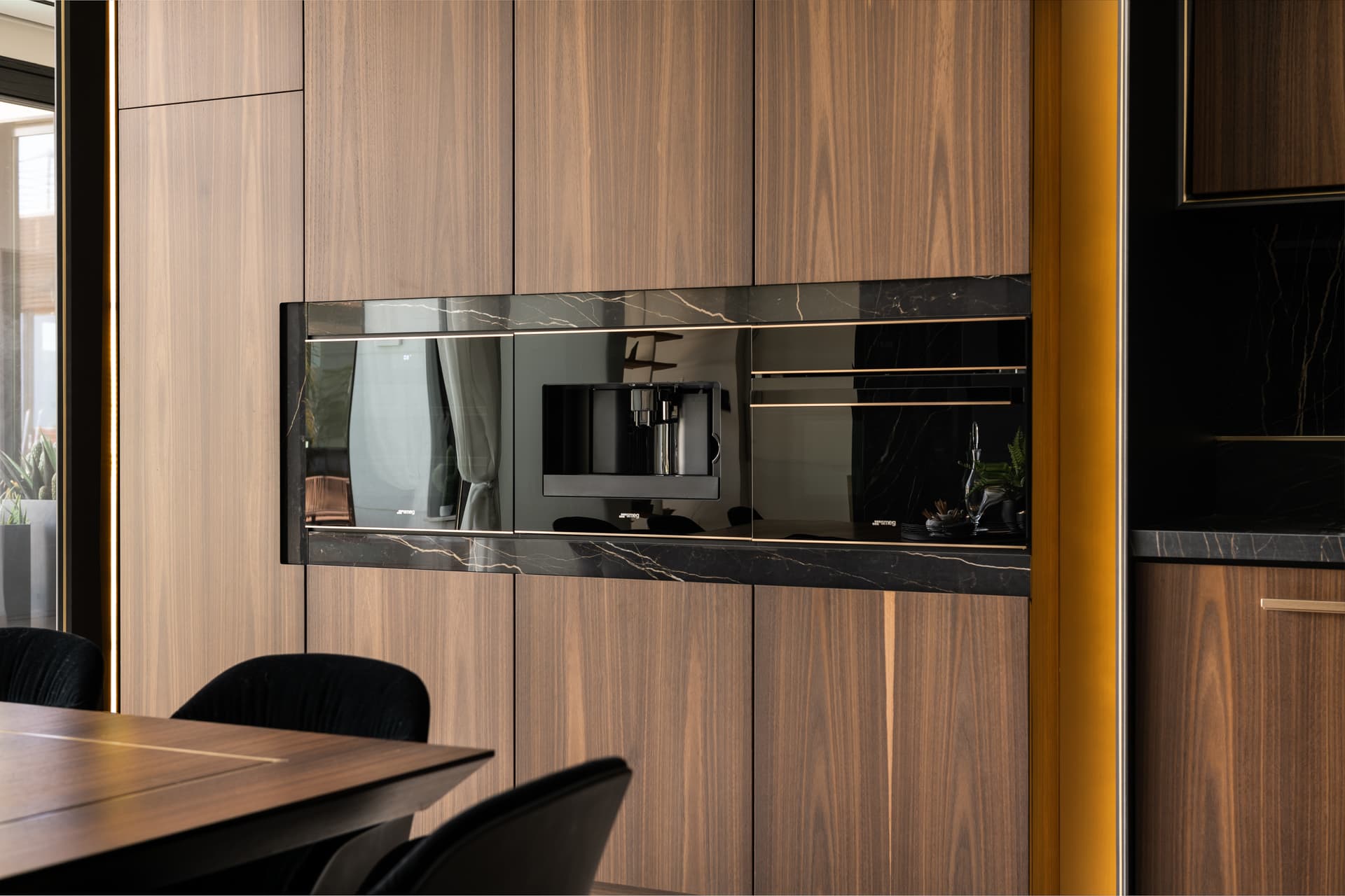 Tall walnut cabinetry with a black veined stone band framing built-in appliances in the kitchen of King David