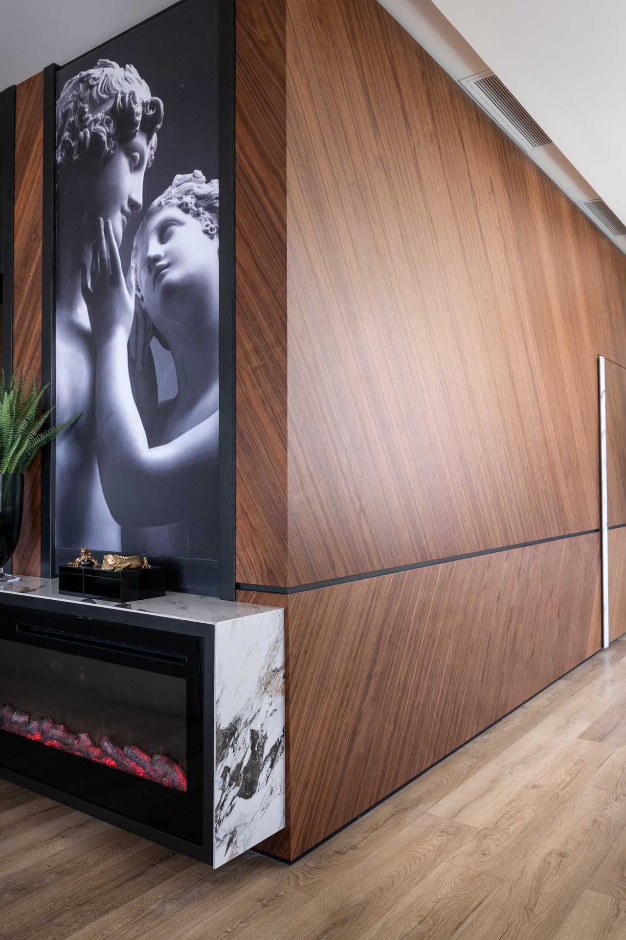 Diagonal walnut wall wrapping past a veined stone fireplace and classical sculpture print in the master bedroom of King David