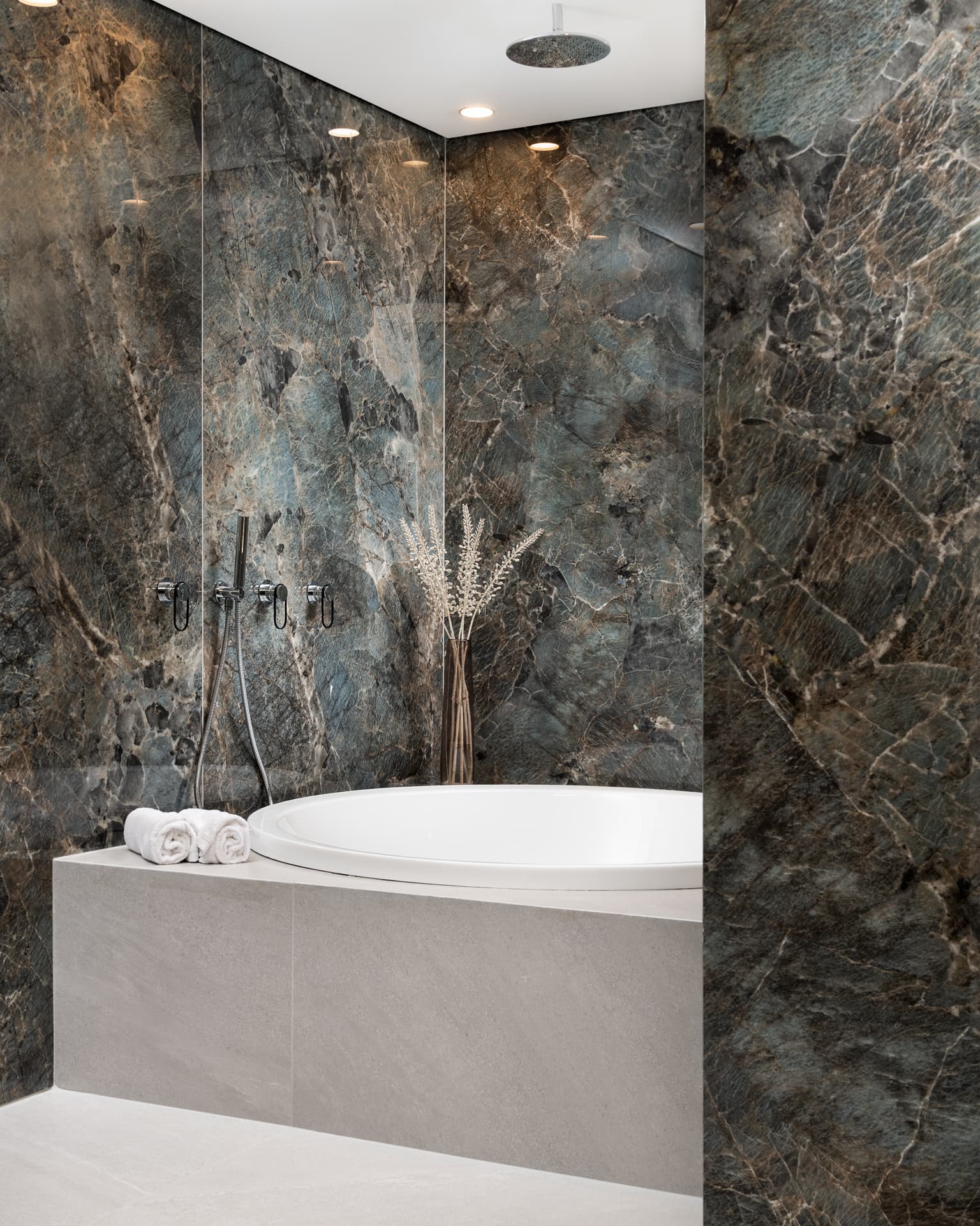 Round white bathtub in a pale stone surround framed by dark blue-green veined stone walls in the bathroom of Marquina