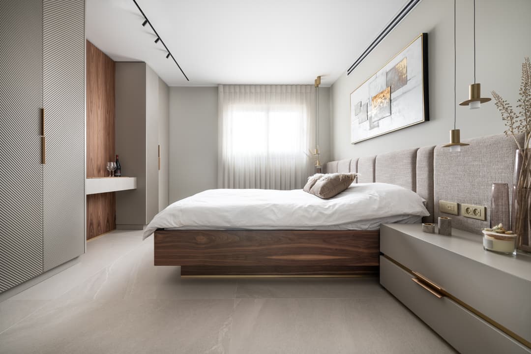 Bedroom view along a diagonally ribbed wardrobe wall toward the walnut bed, sheer curtains and a walnut-lined desk niche in Marquina