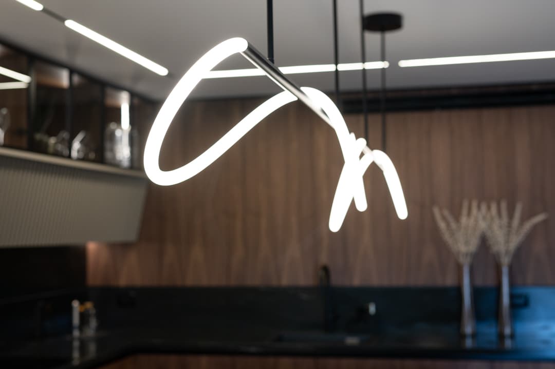 Looped LED pendant light in front of walnut wall panelling and the black stone counter of the kitchen in Marquina