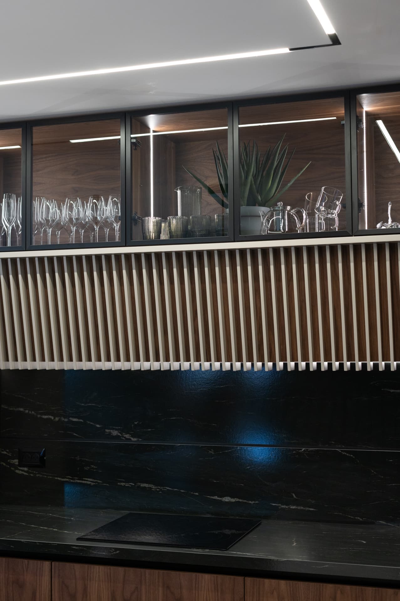 Black-framed glass cabinets with glassware above a slatted pale panel and black stone backsplash in the kitchen of Marquina