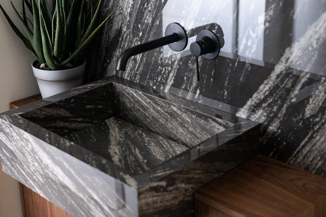 Tight side view of the black streaked stone basin's sloped interior and matte black tap in the powder room of Marquina