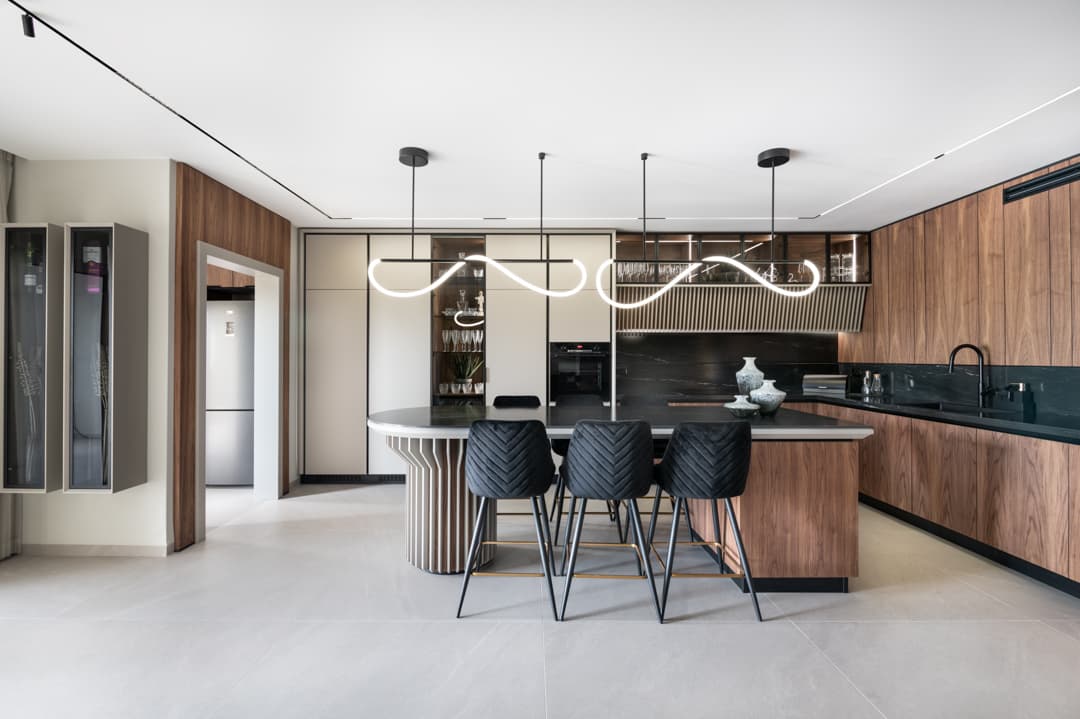 Kitchen with wave-shaped LED pendants over a fluted-base island, black chevron bar stools and walnut cabinetry in Marquina