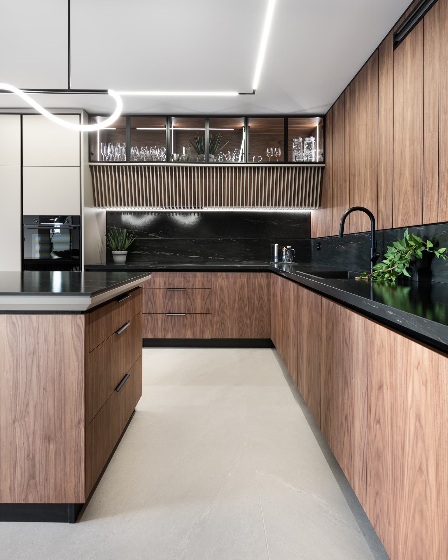 Walnut L-shaped counter run with a black veined stone backsplash and glass-front upper cabinets in the kitchen of Marquina