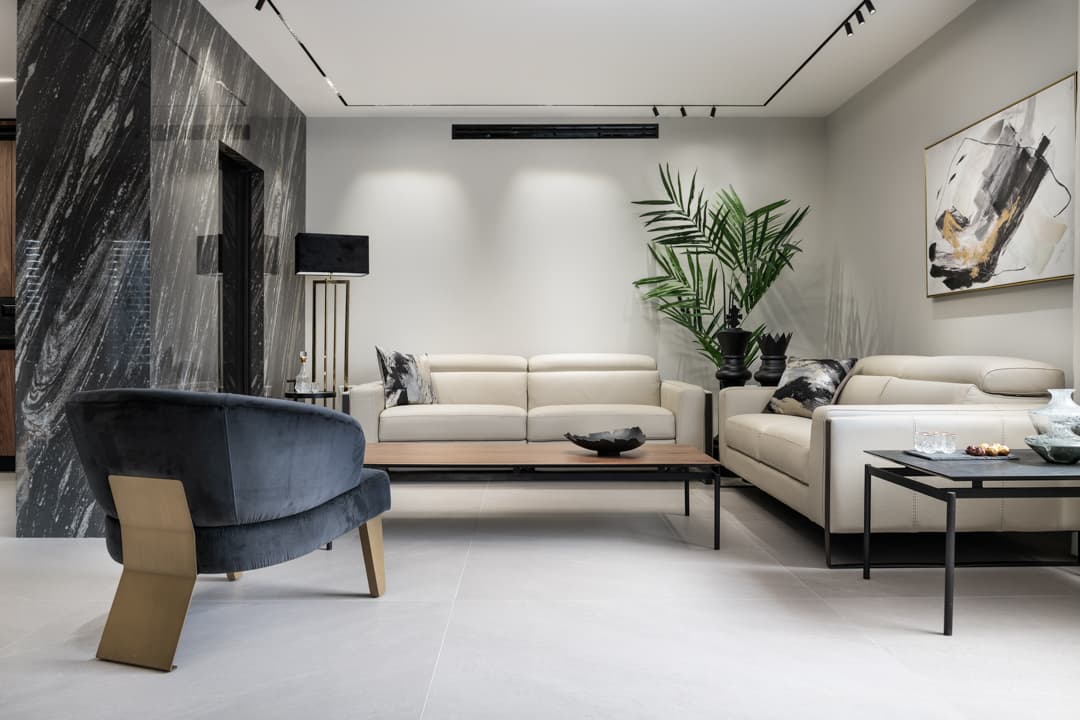 Cream leather sofas, a walnut coffee table and a navy velvet armchair beside the streaked black stone wall in the living room of Marquina