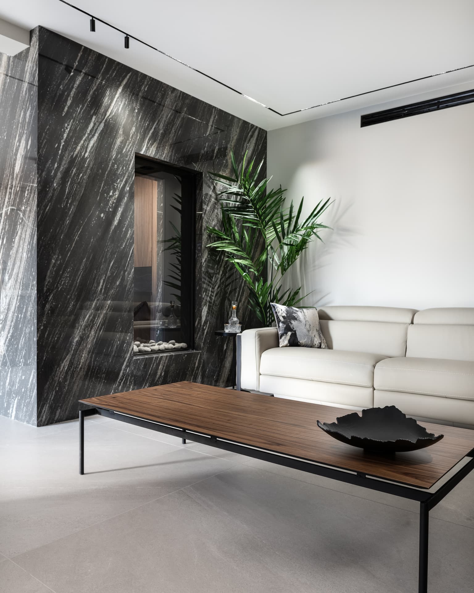 Fireplace niche set in a streaked black stone wall beside a walnut coffee table in the living room of Marquina