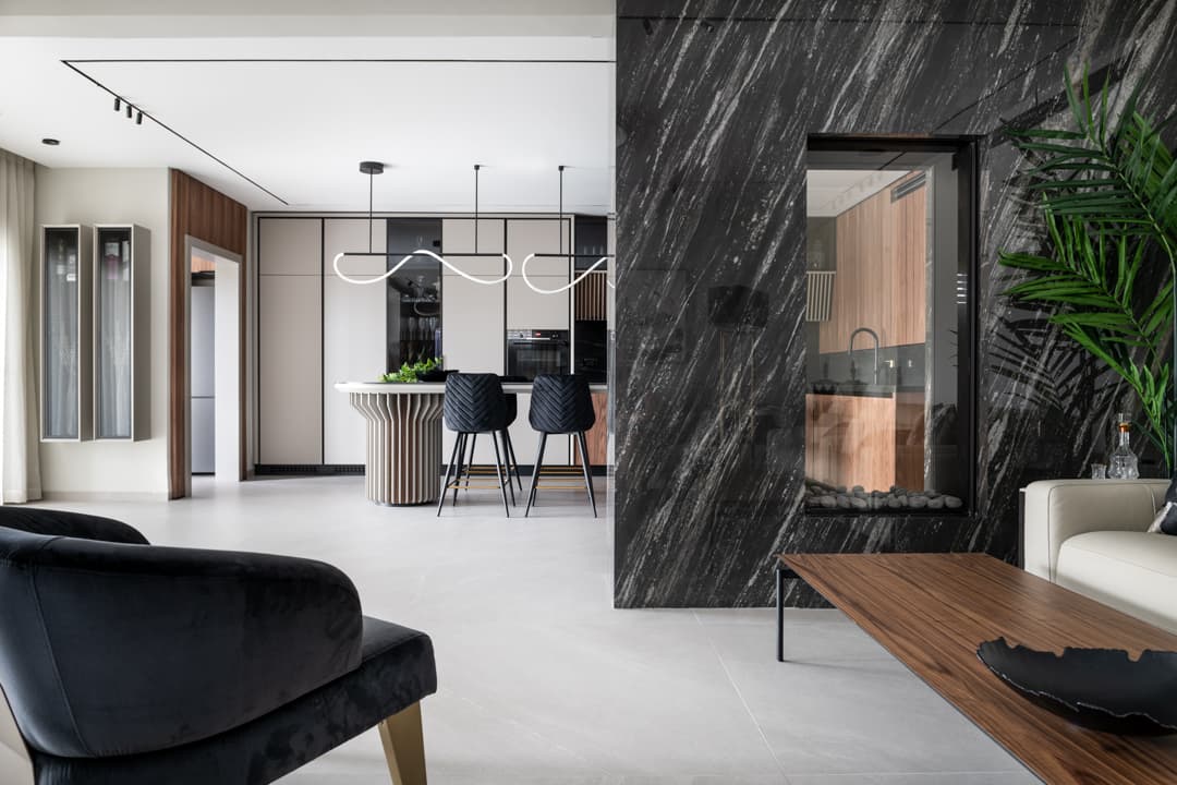 View from the living room past the black stone fireplace toward the kitchen island and stools in Marquina