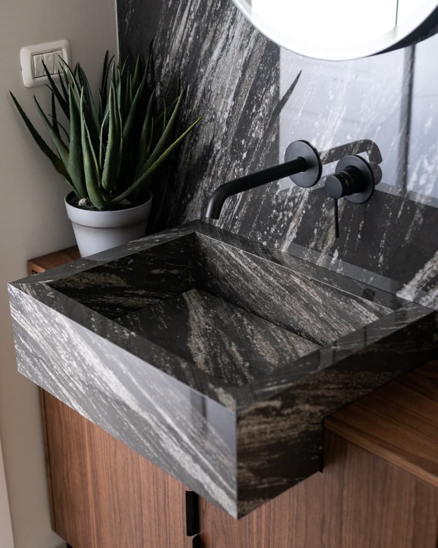 Angled close-up of the black streaked stone basin and matte black wall-mounted tap beside an aloe in the powder room of Marquina