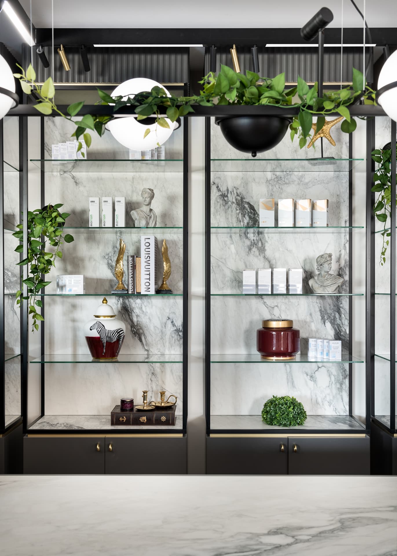 Glass shelves with veined stone backs, trailing greenery and a globe pendant in the reception display of Moeen Clinic