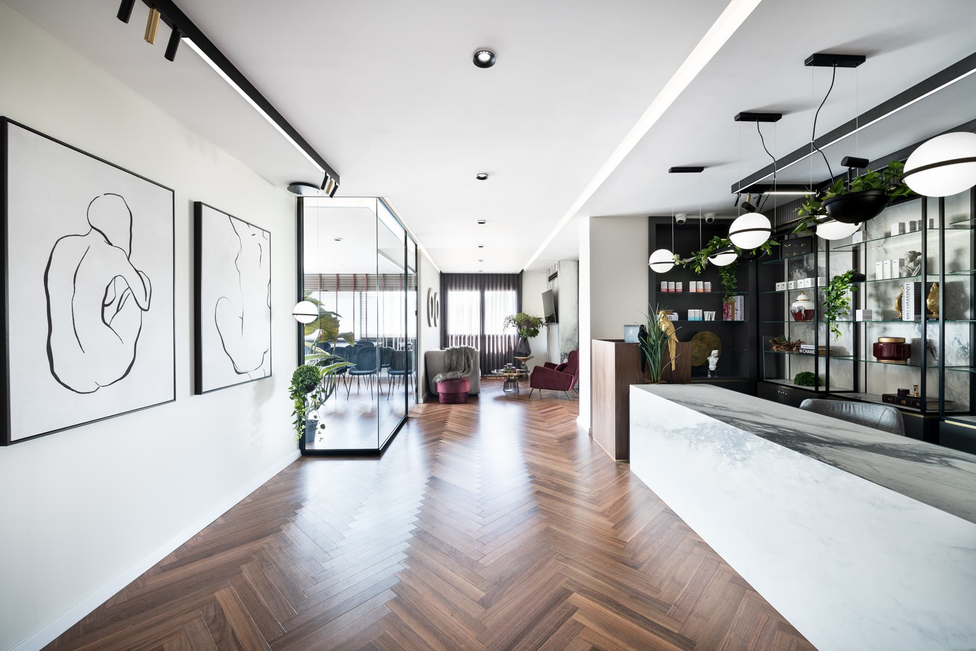 Long herringbone corridor with line-drawing artworks, a glass-walled room and the stone reception desk in the hallway of Moeen Clinic
