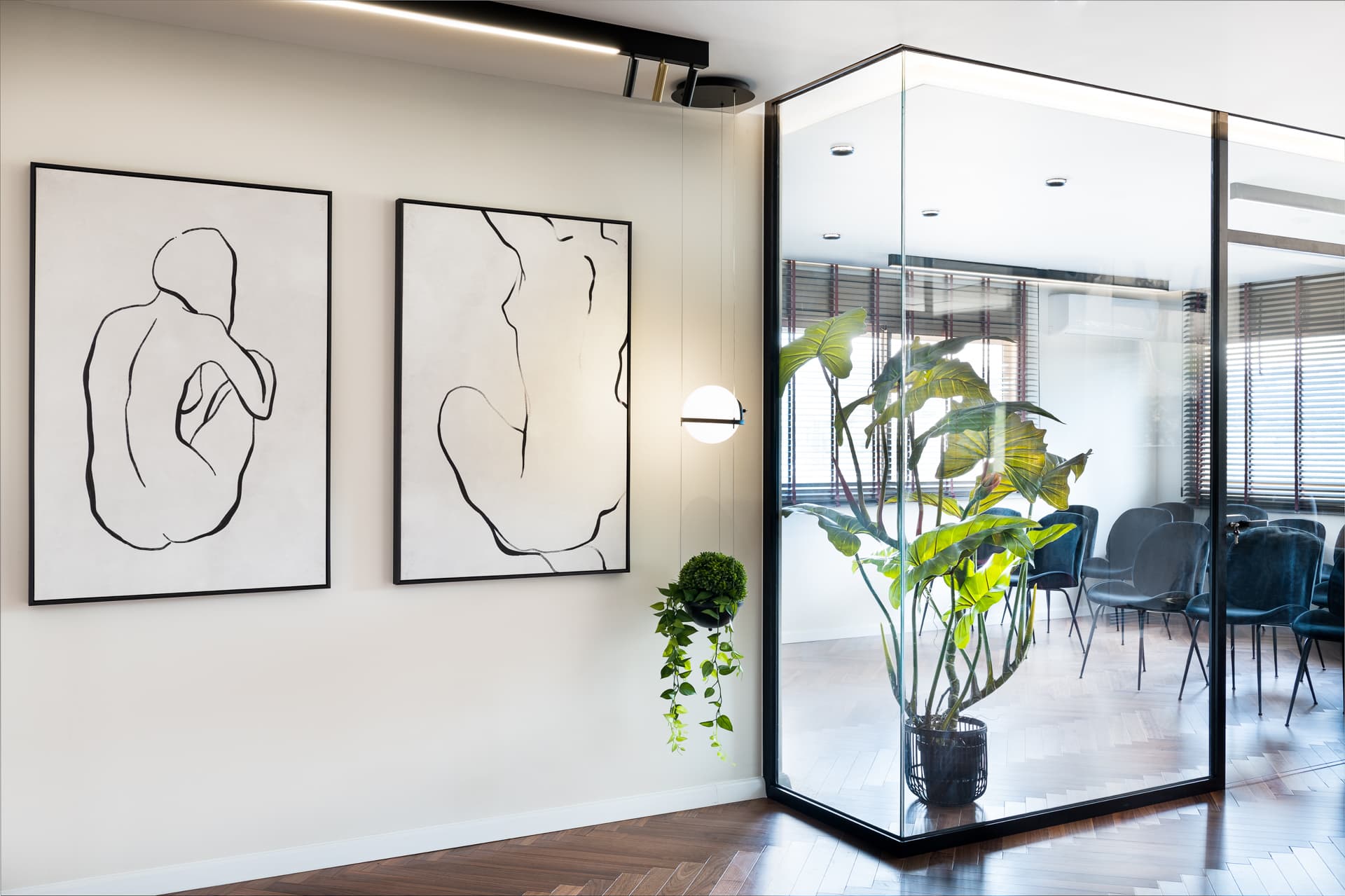 Pair of framed line-drawing figure artworks beside a glass-cornered room with rows of dark chairs in the hallway of Moeen Clinic