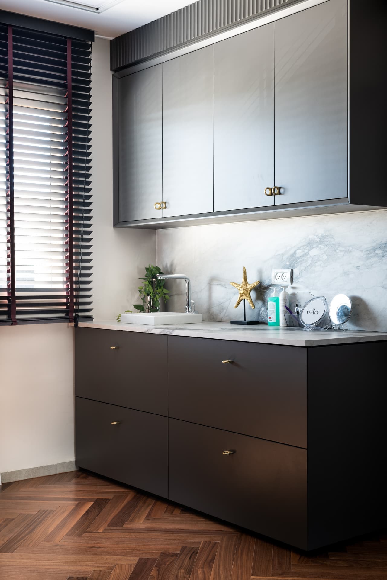 Charcoal cabinetry with brass knobs, a veined stone backsplash and a white vessel sink in the prep area of Moeen Clinic