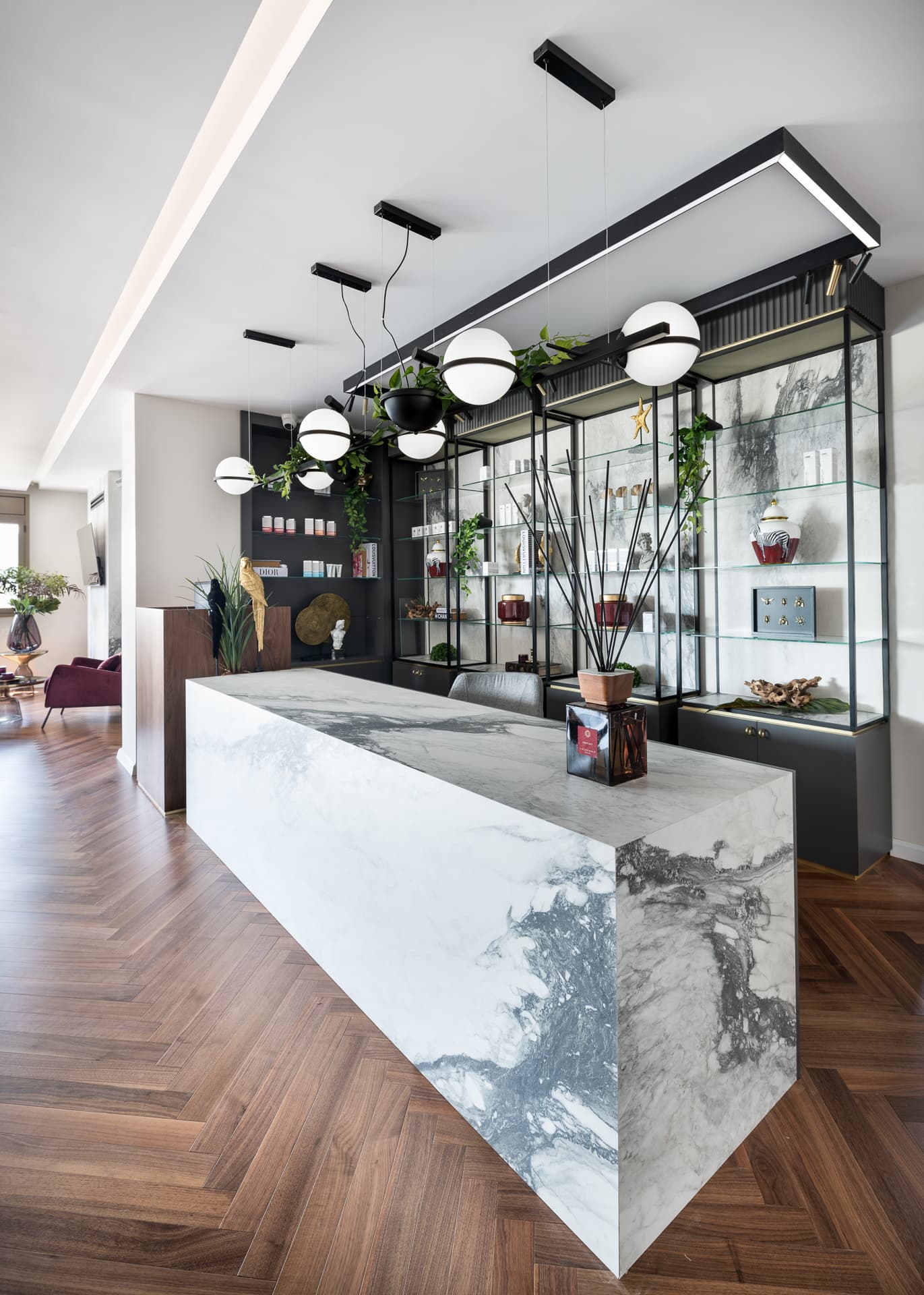 Angled view of the waterfall-edge veined stone desk under globe pendants and a planted rail in the reception of Moeen Clinic