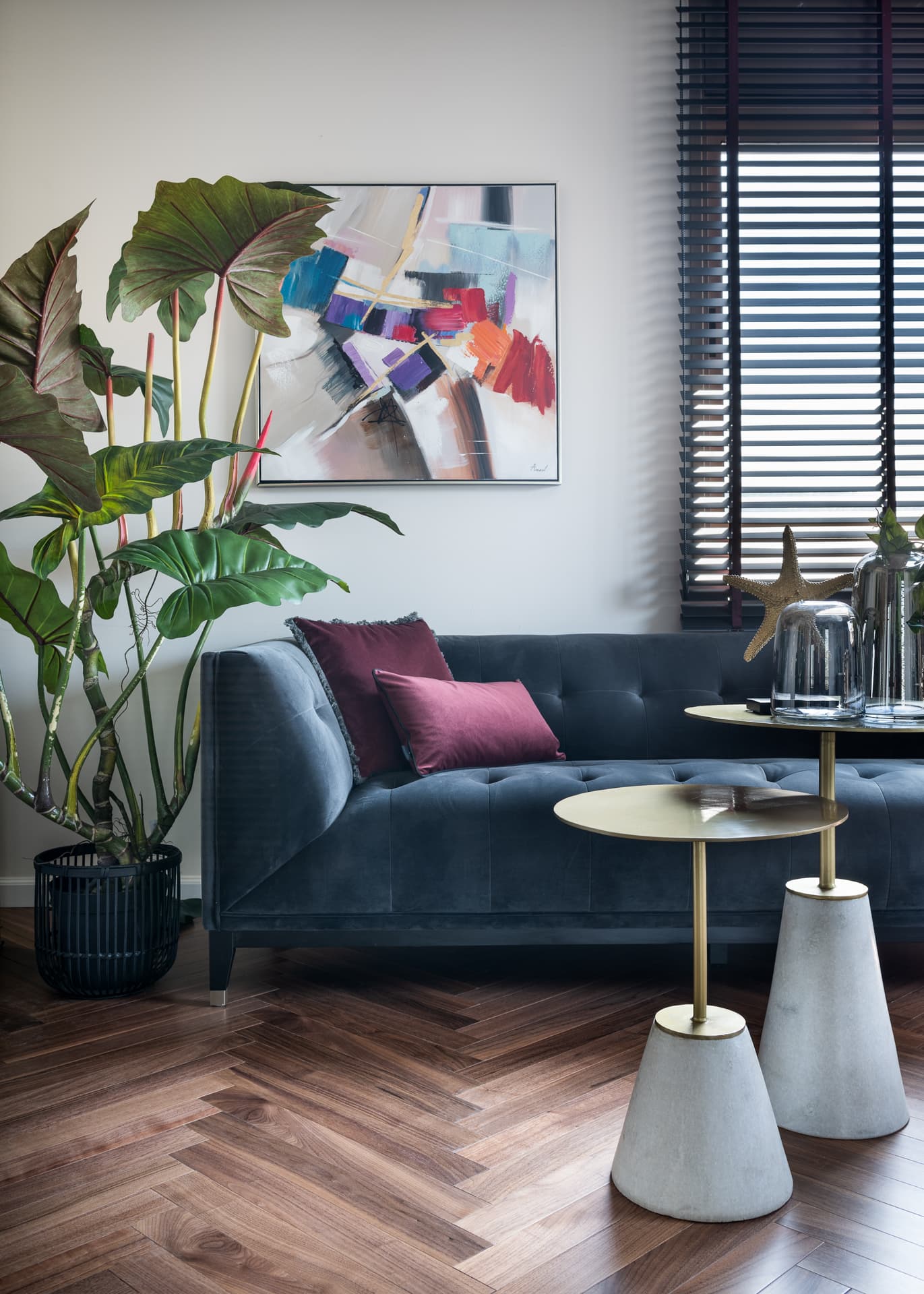 Tufted blue velvet sofa with plum cushions and brass-topped cone side tables under abstract art in the treatment room of Moeen Clinic