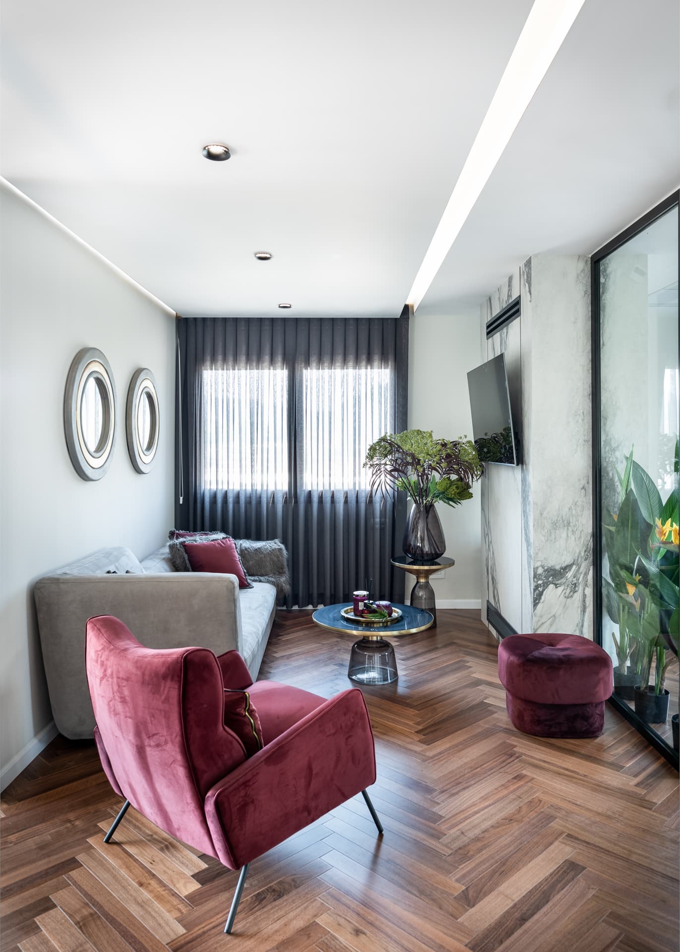 Plum velvet armchair, grey sofa and round framed mirrors beside a veined stone column in the waiting lounge of Moeen Clinic