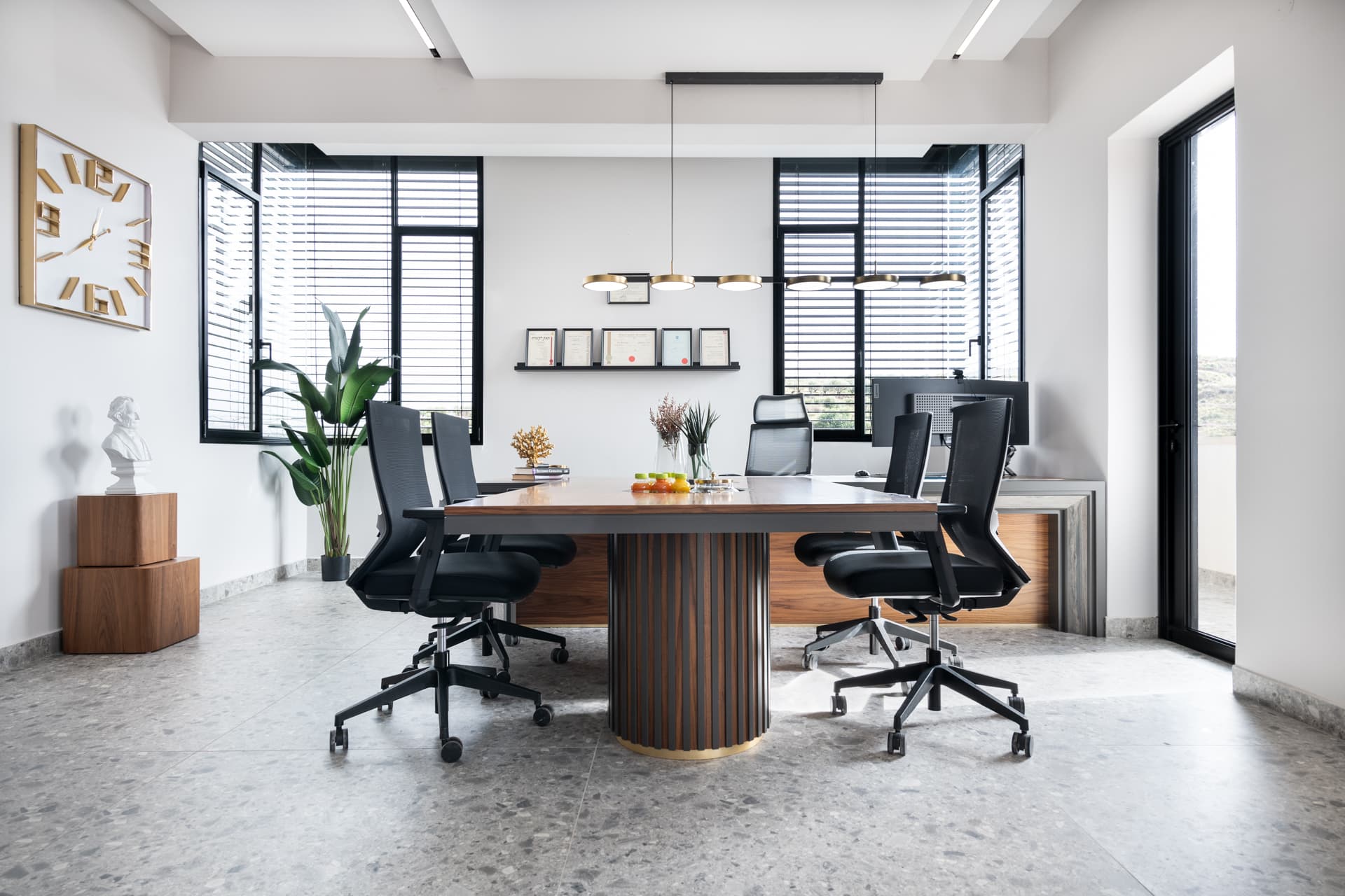 Meeting table on a fluted walnut drum base with black mesh chairs and a brass disc pendant in the office conference room