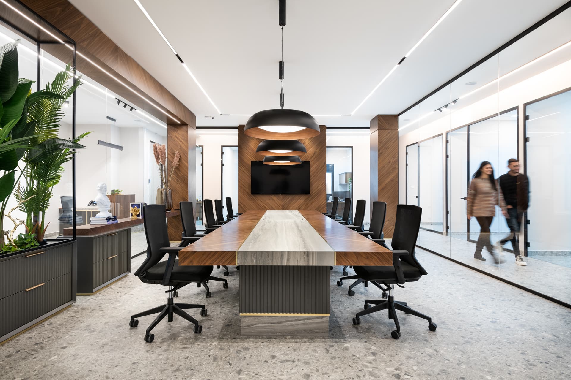Long walnut boardroom table with a veined stone centre strip under three black dome pendants in the office conference room