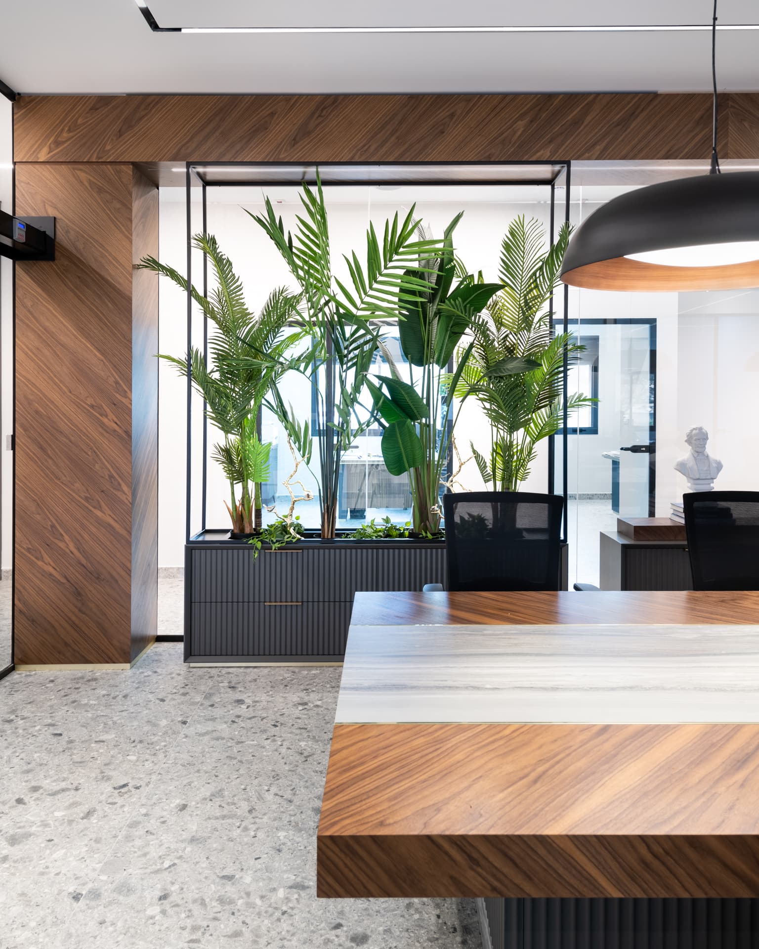 Black steel-framed planter screen with palms above fluted cabinets beside the walnut table edge in the office conference room