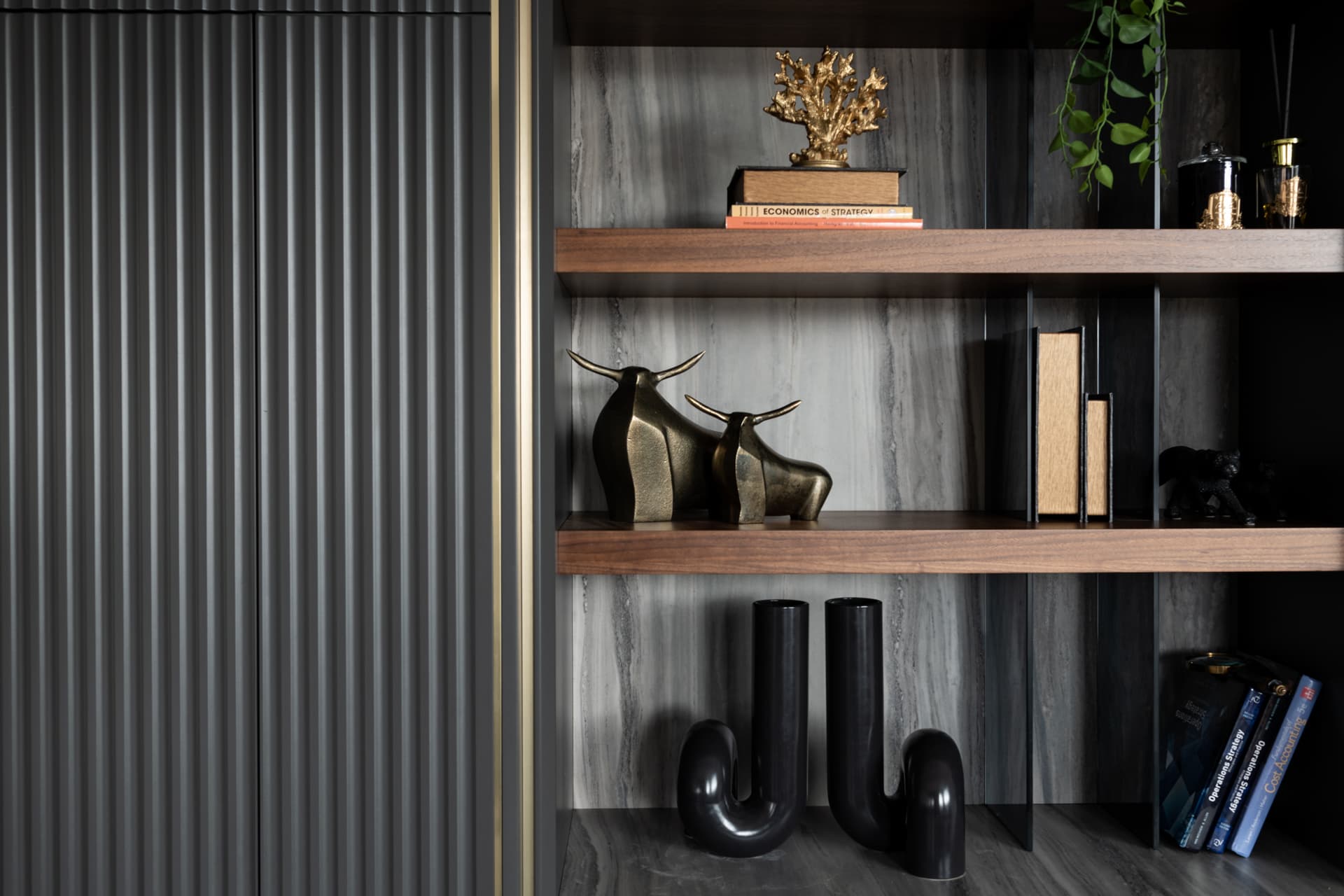 Brass bull sculptures and black tubular vases on walnut shelves against grey veined stone in the executive office